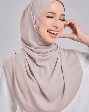 Woman wearing a beige hijab against a plain background