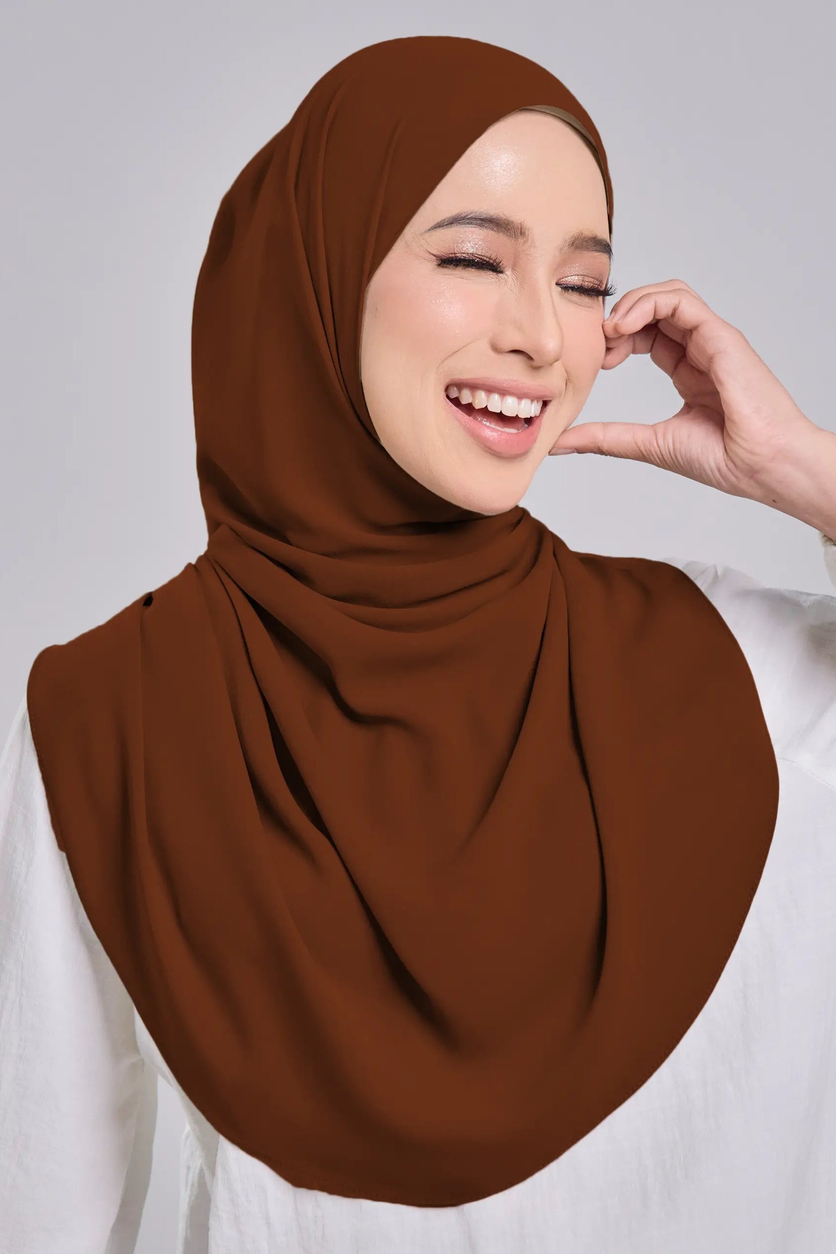 Woman wearing a brown hijab against a gray background