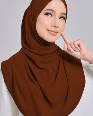 Woman wearing a brown hijab and white top against a gray background