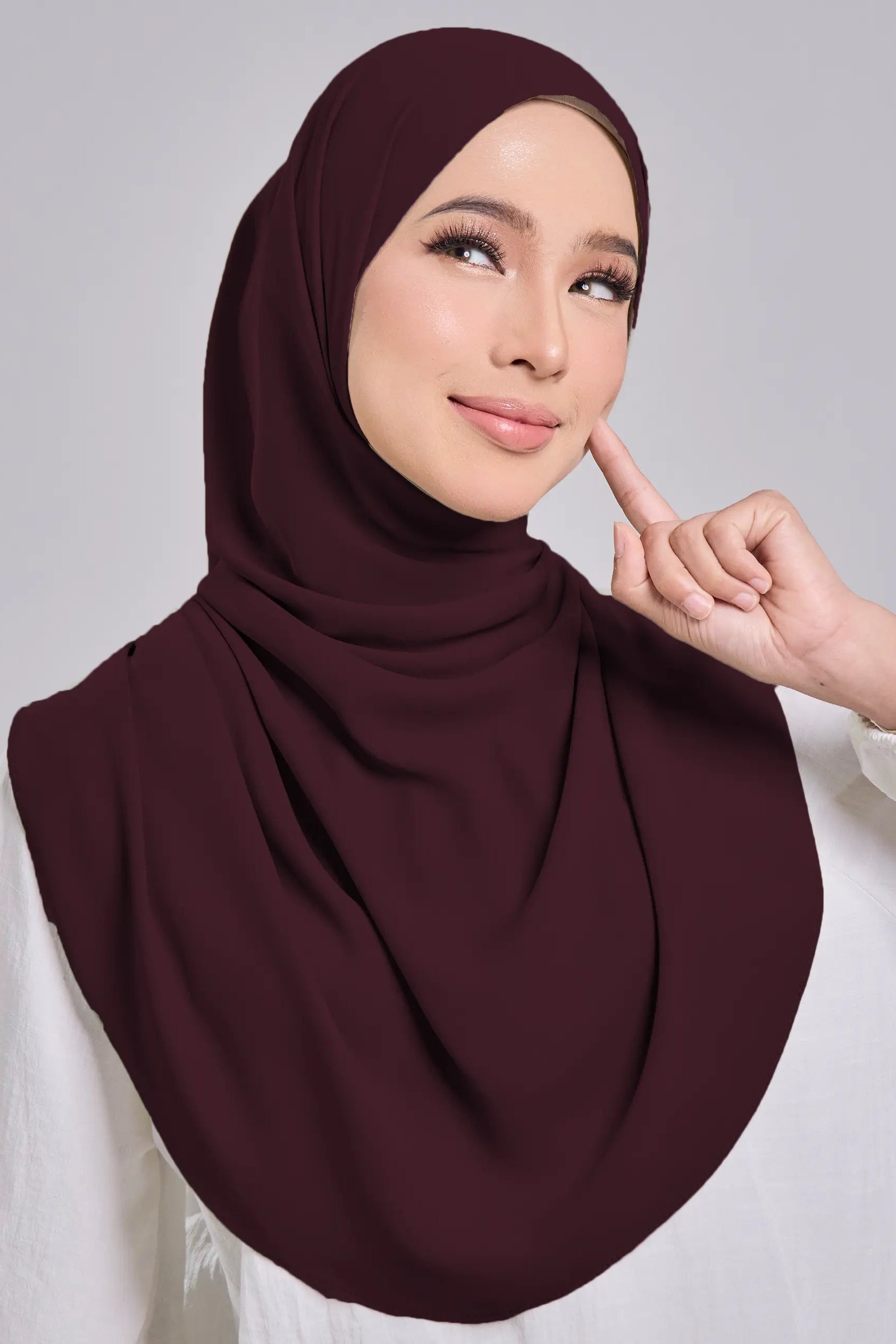 Woman wearing a brown hijab and white top on a gray background