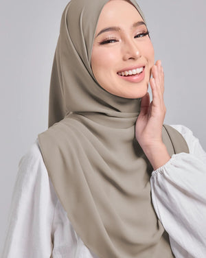 Woman wearing a beige hijab and white top against a gray background