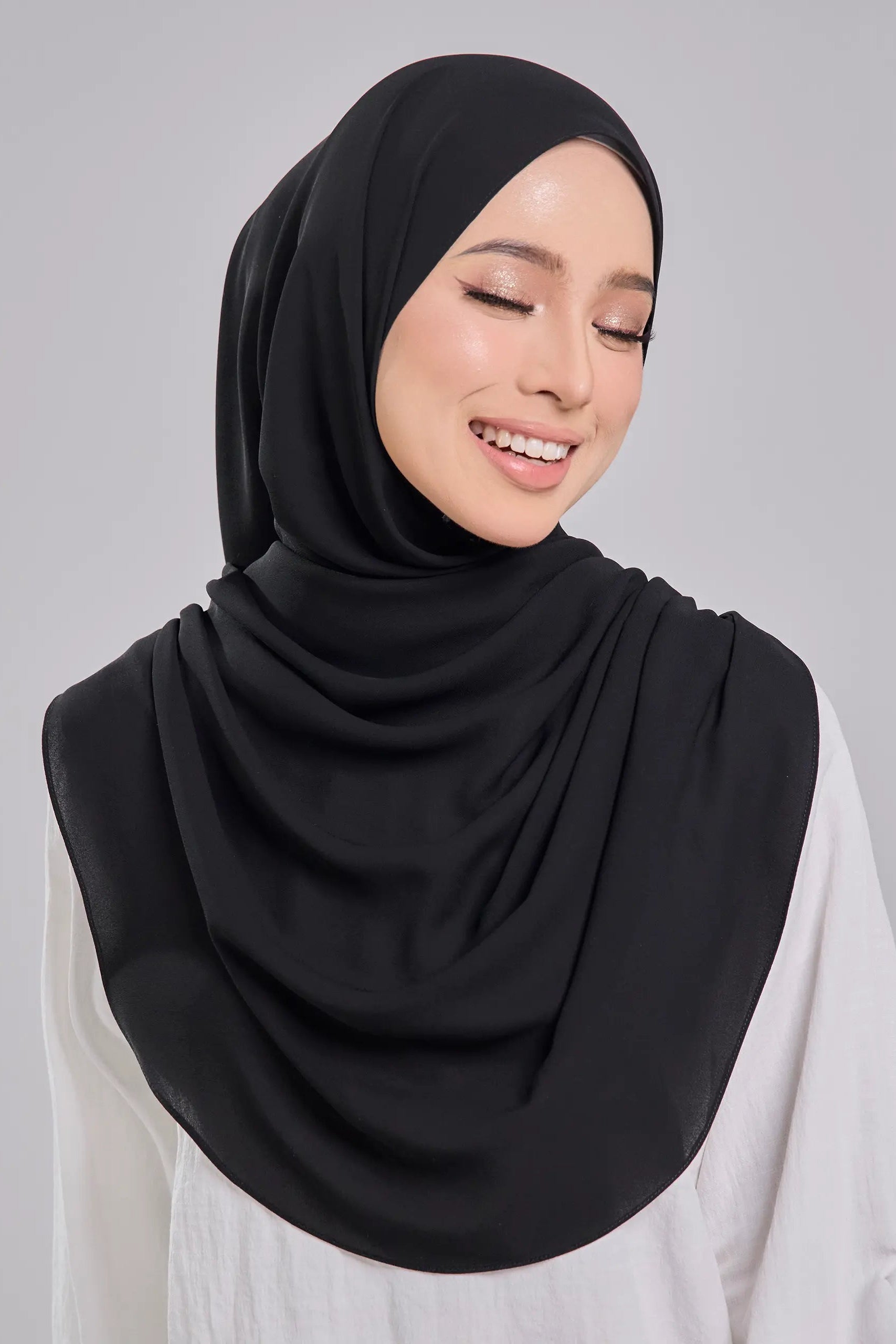 Woman wearing a black hijab and white top on a gray background