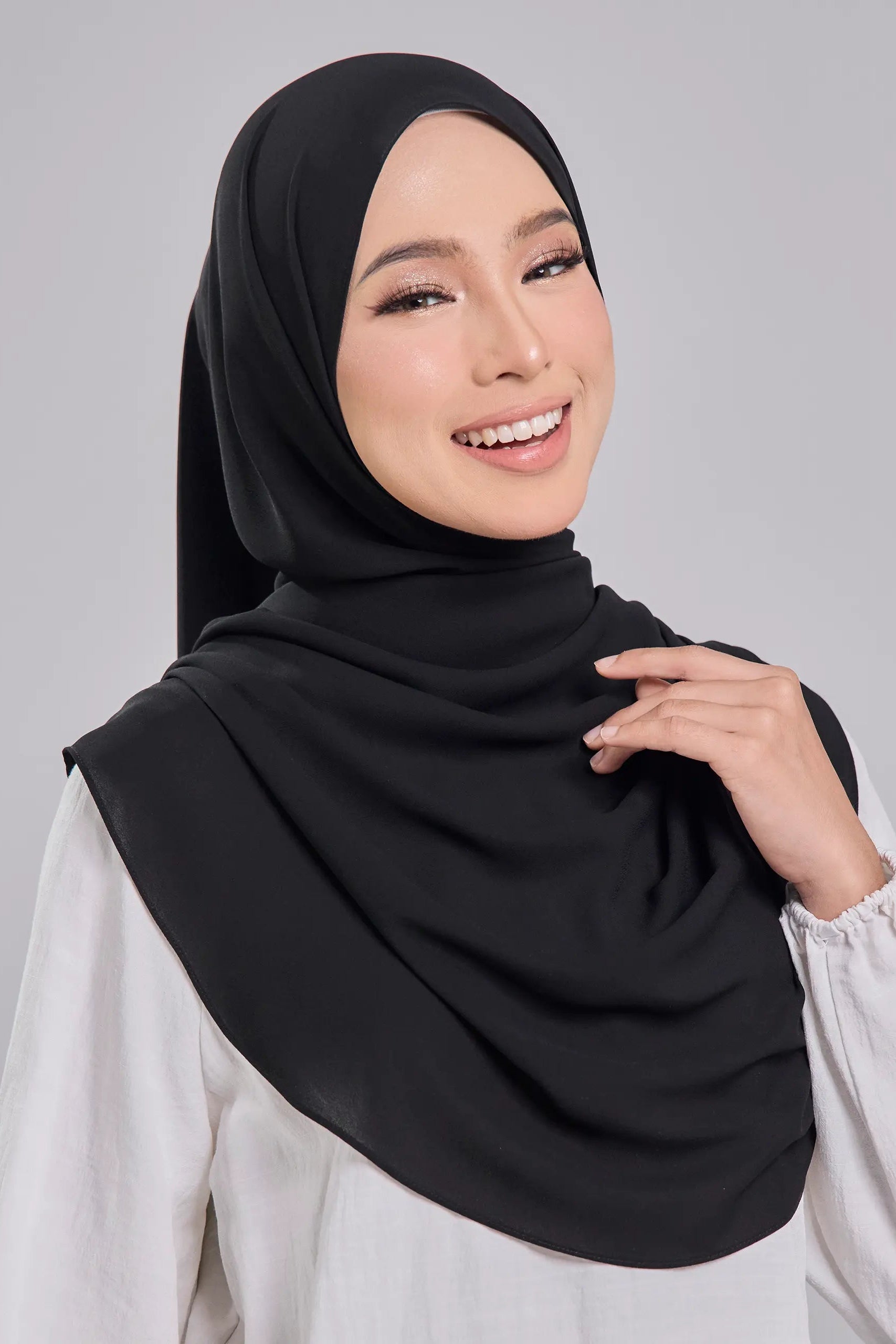Woman wearing a black hijab and white blouse against a gray background