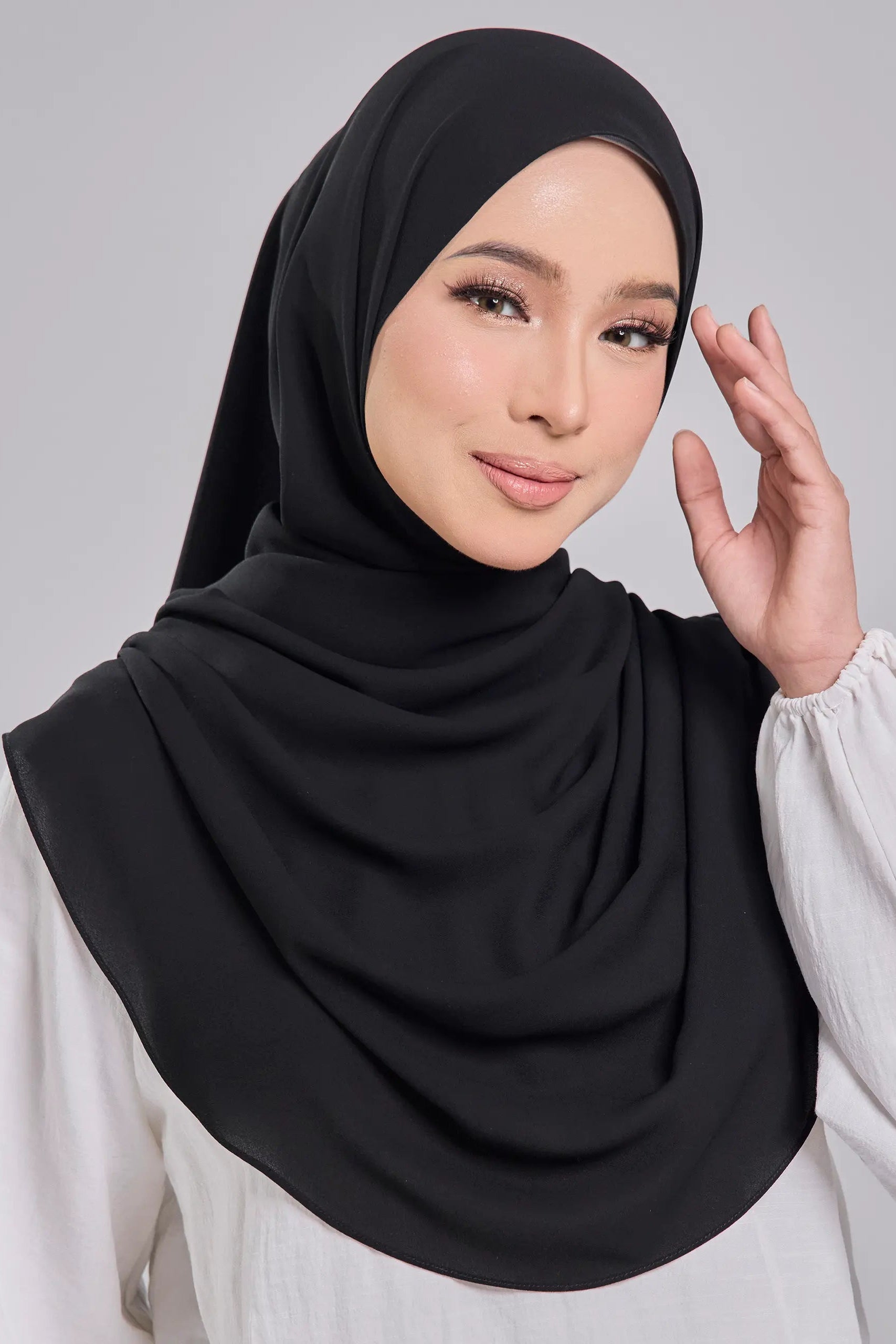 Woman wearing a black hijab and white top on a gray background