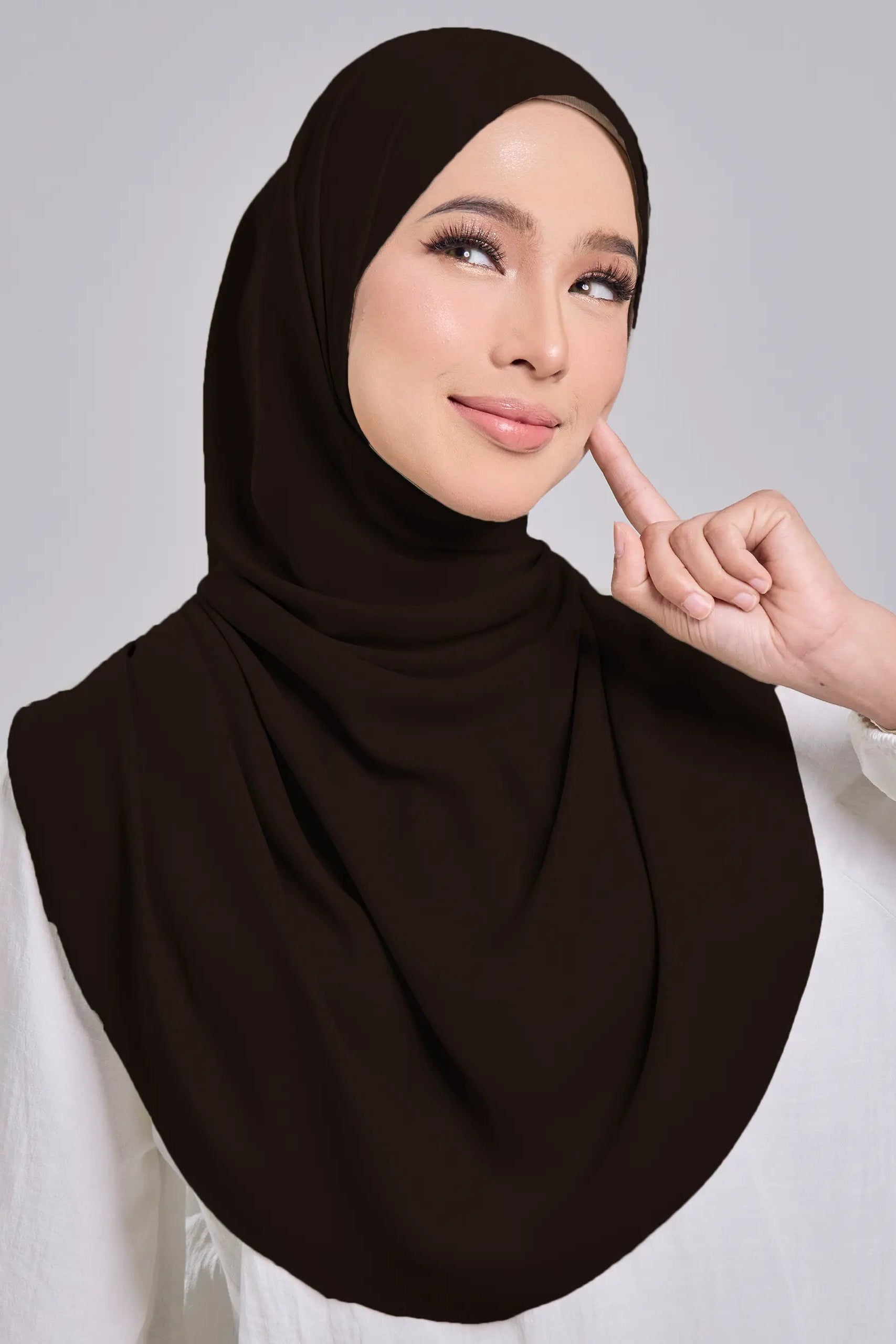 Woman wearing a brown hijab and white blouse against a gray background