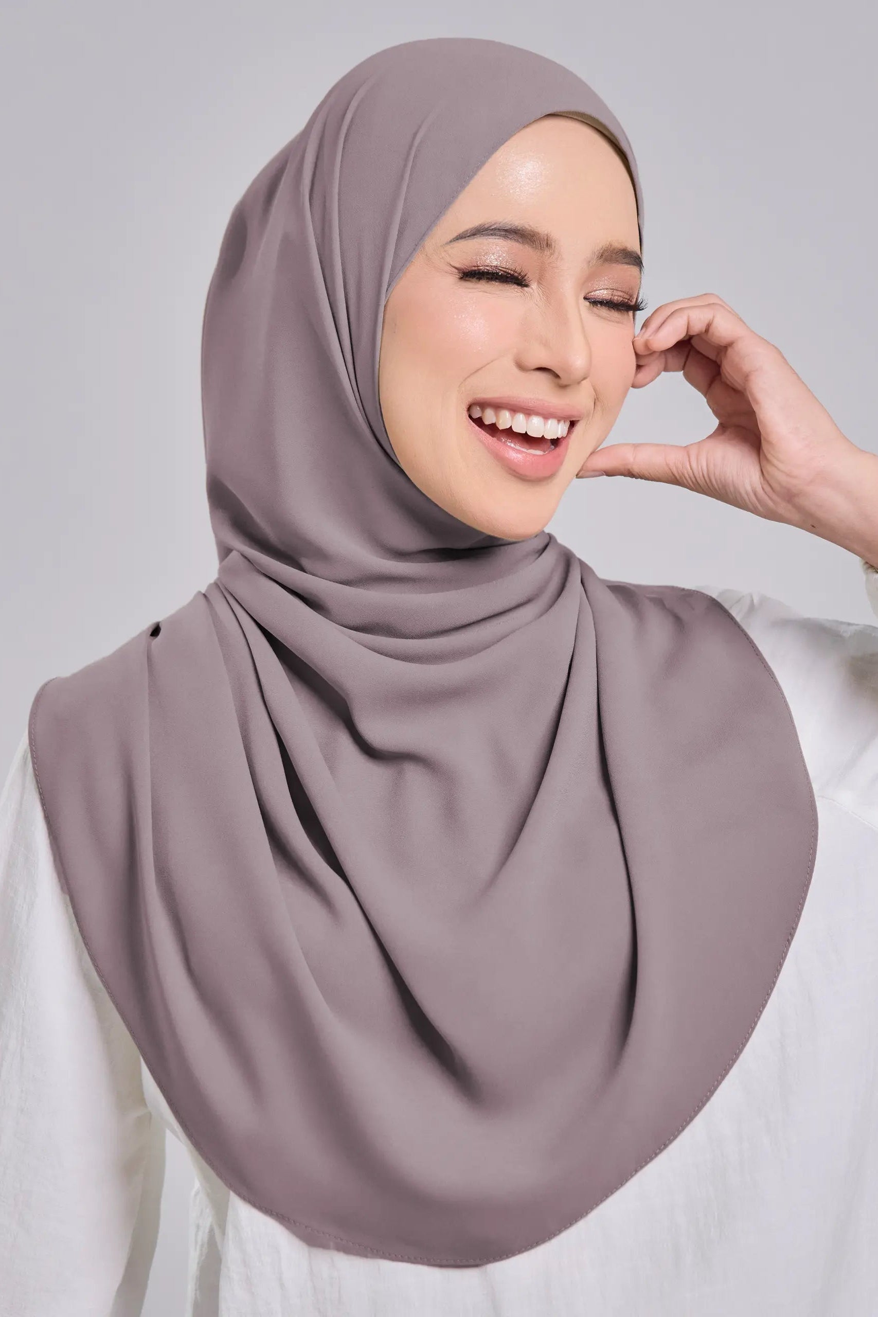 Woman wearing a light brown hijab against a gray background