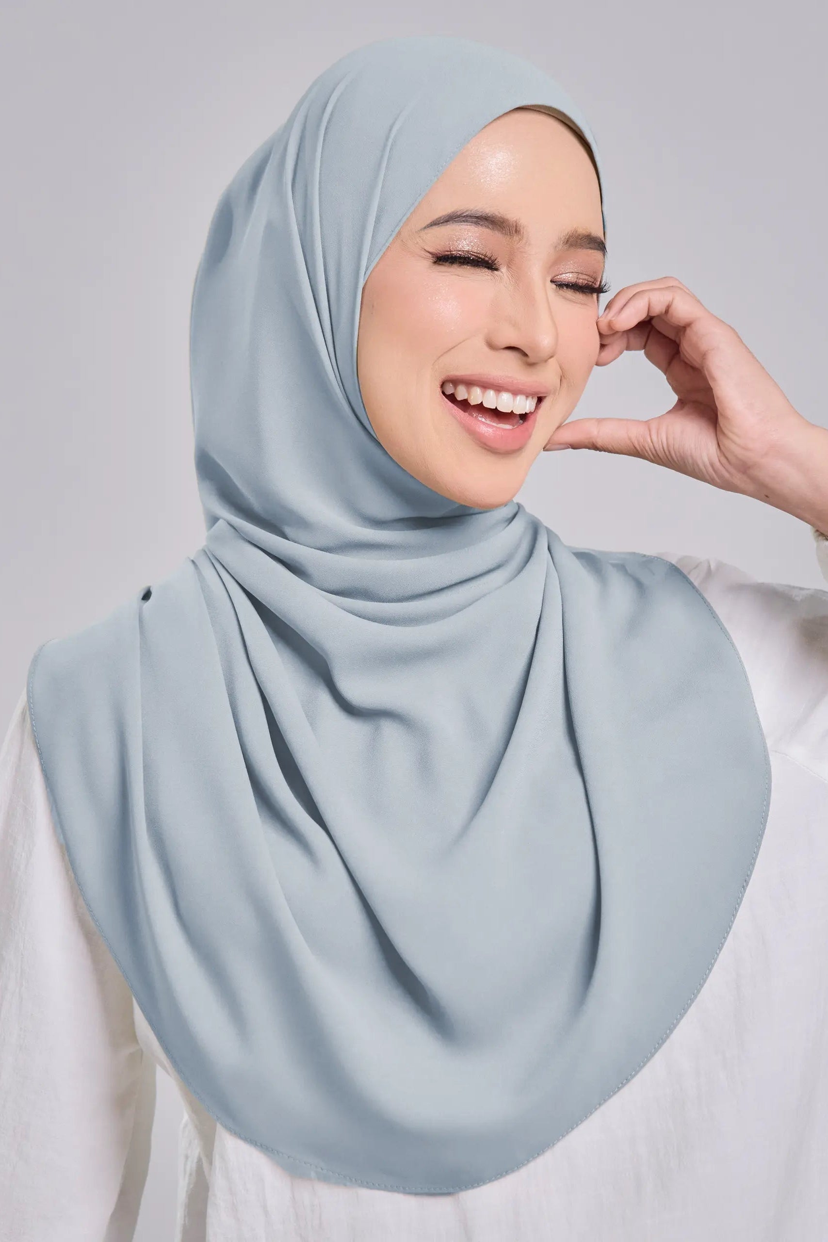Woman wearing a light blue hijab against a gray background