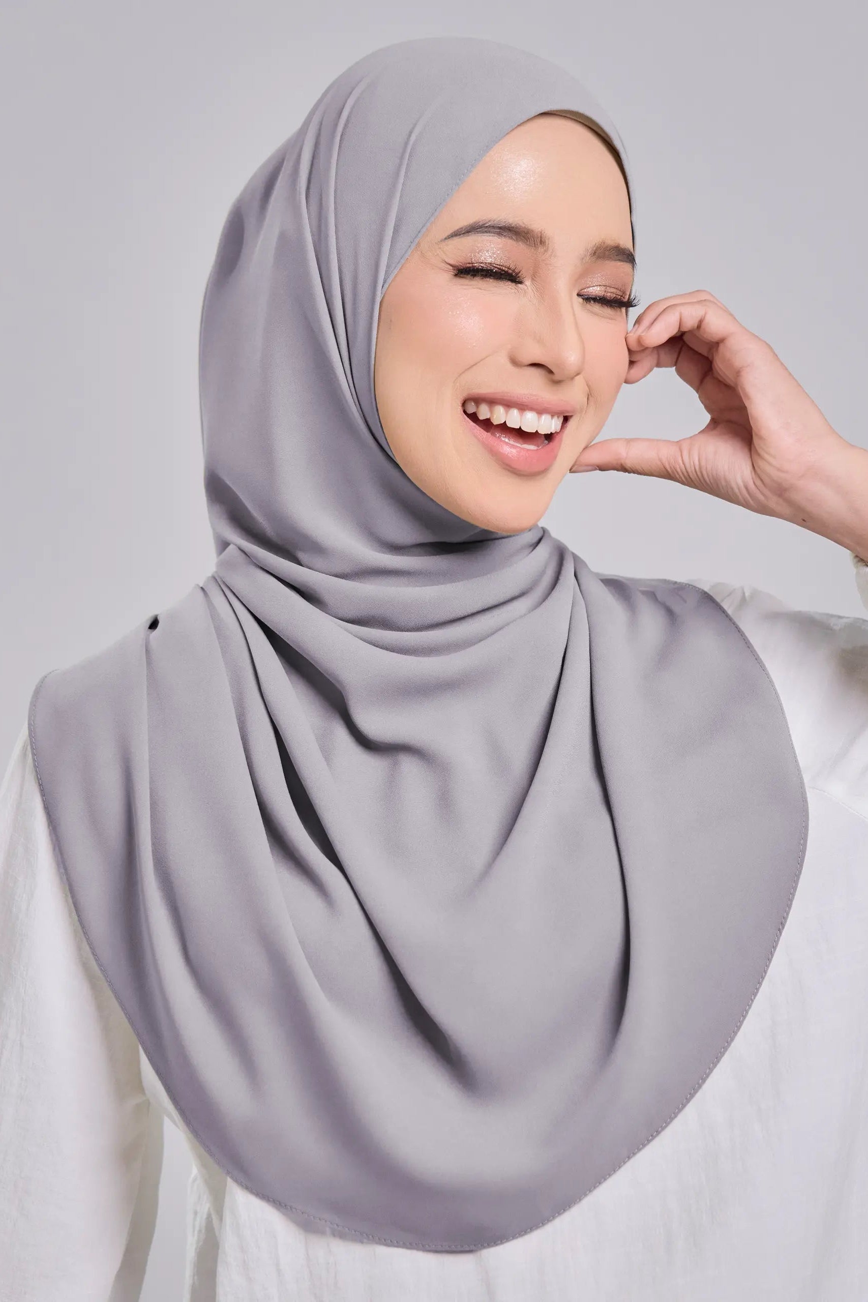 Woman wearing a light gray hijab against a plain background