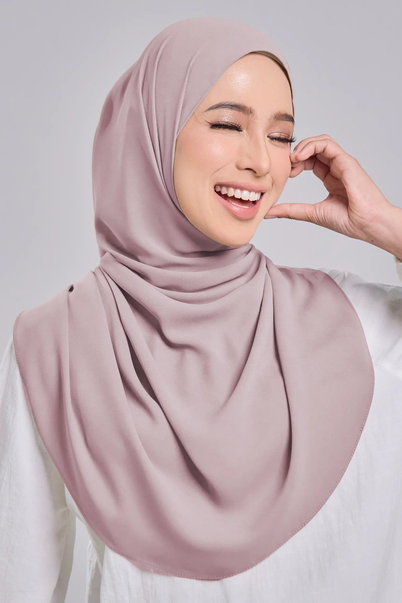 Woman wearing a light pink hijab against a plain background