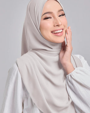 Woman wearing a light gray hijab and white top against a plain background