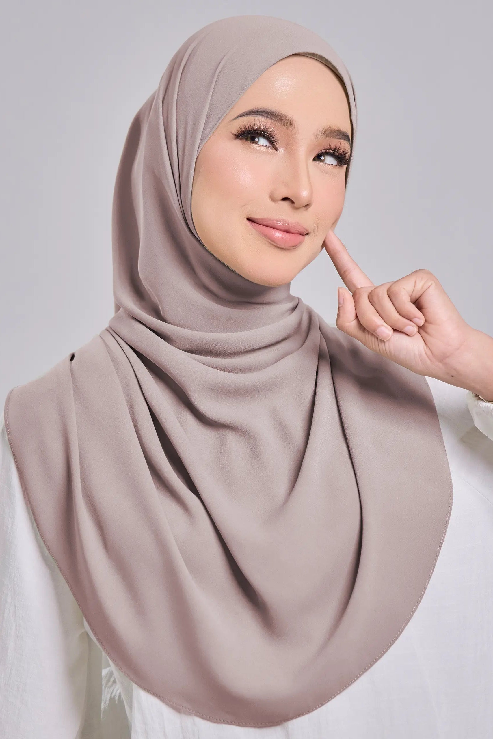 Woman wearing a beige hijab against a gray background