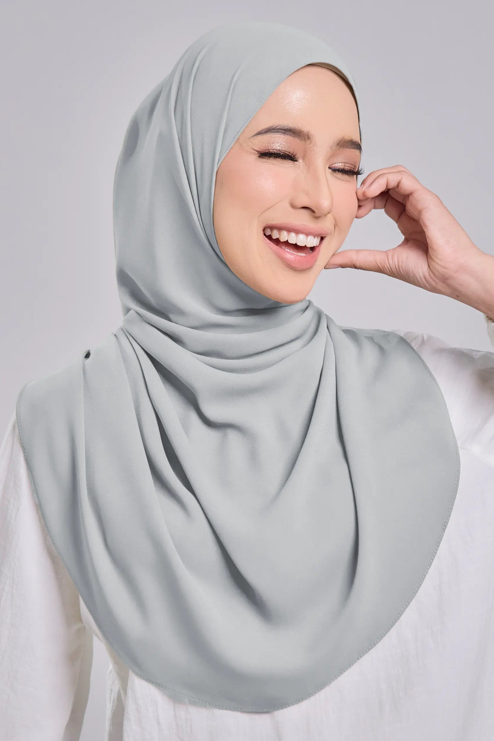 Woman wearing a light gray hijab against a plain background