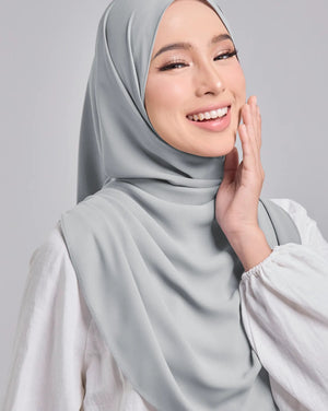 Woman wearing a light gray hijab and white shirt on a gray background