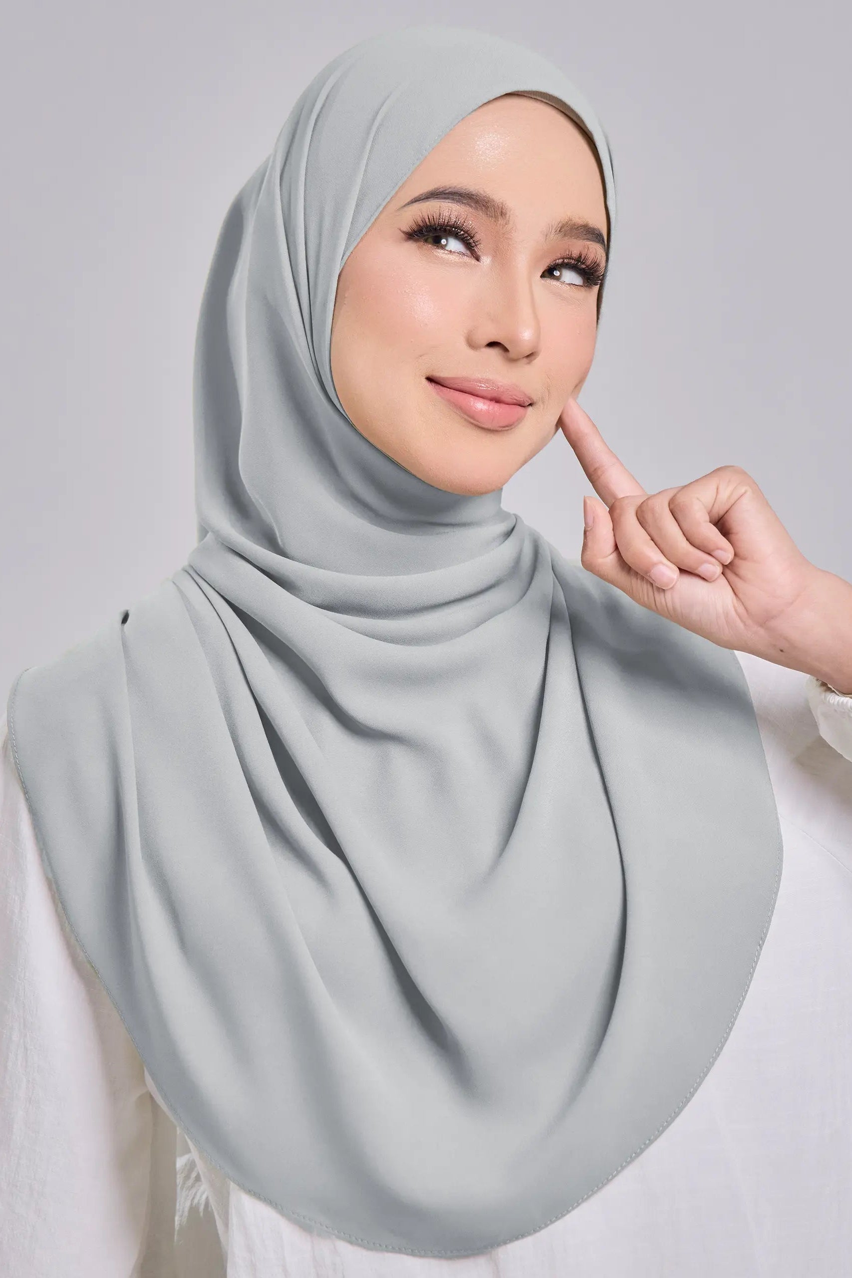 Woman wearing a light gray hijab with a neutral background