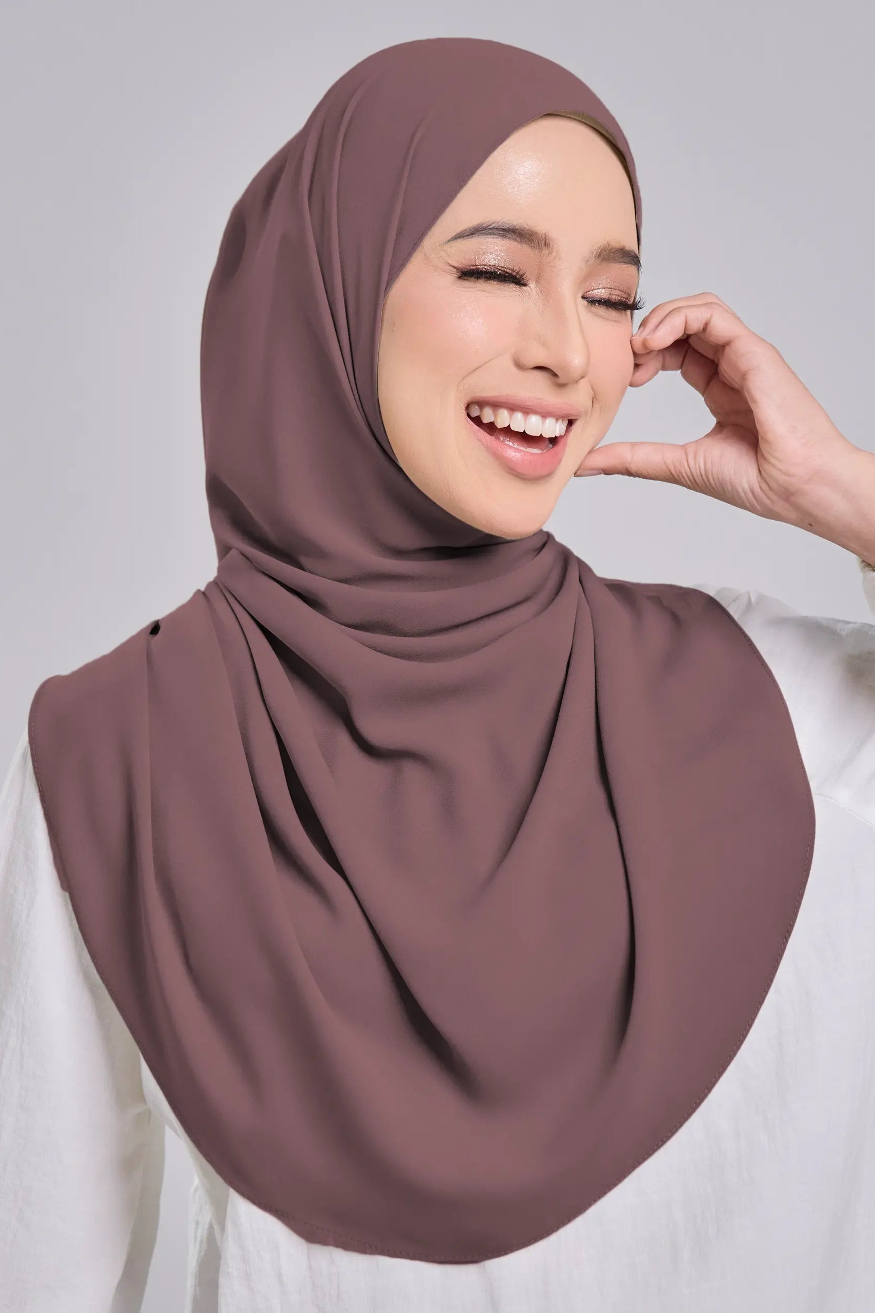 Woman wearing a brown hijab and white shirt against a gray background