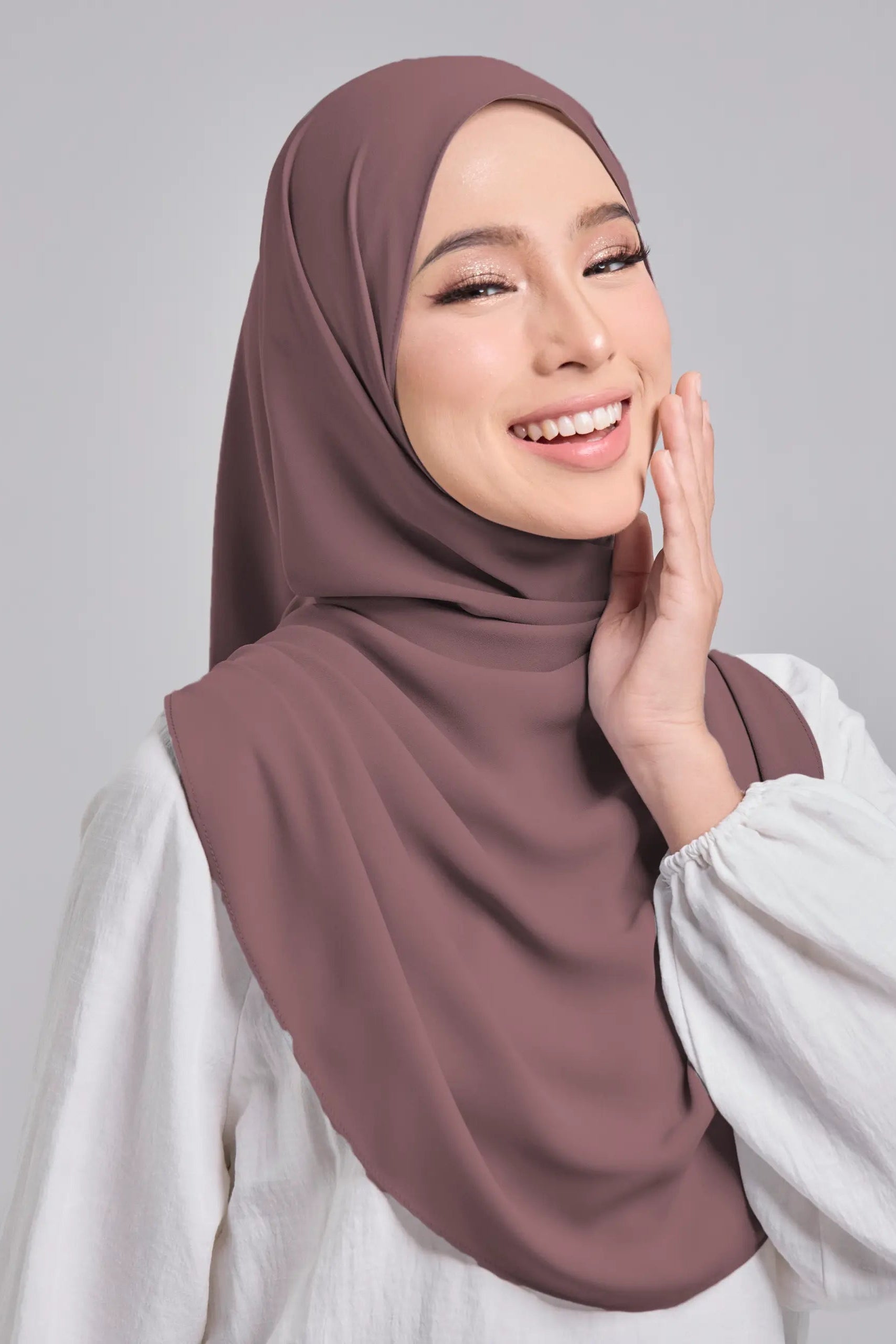 Woman wearing a brown hijab and white shirt on a gray background