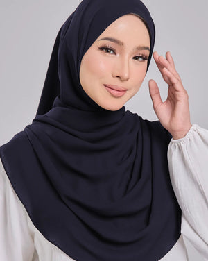 Woman wearing a navy hijab and white blouse against a gray background
