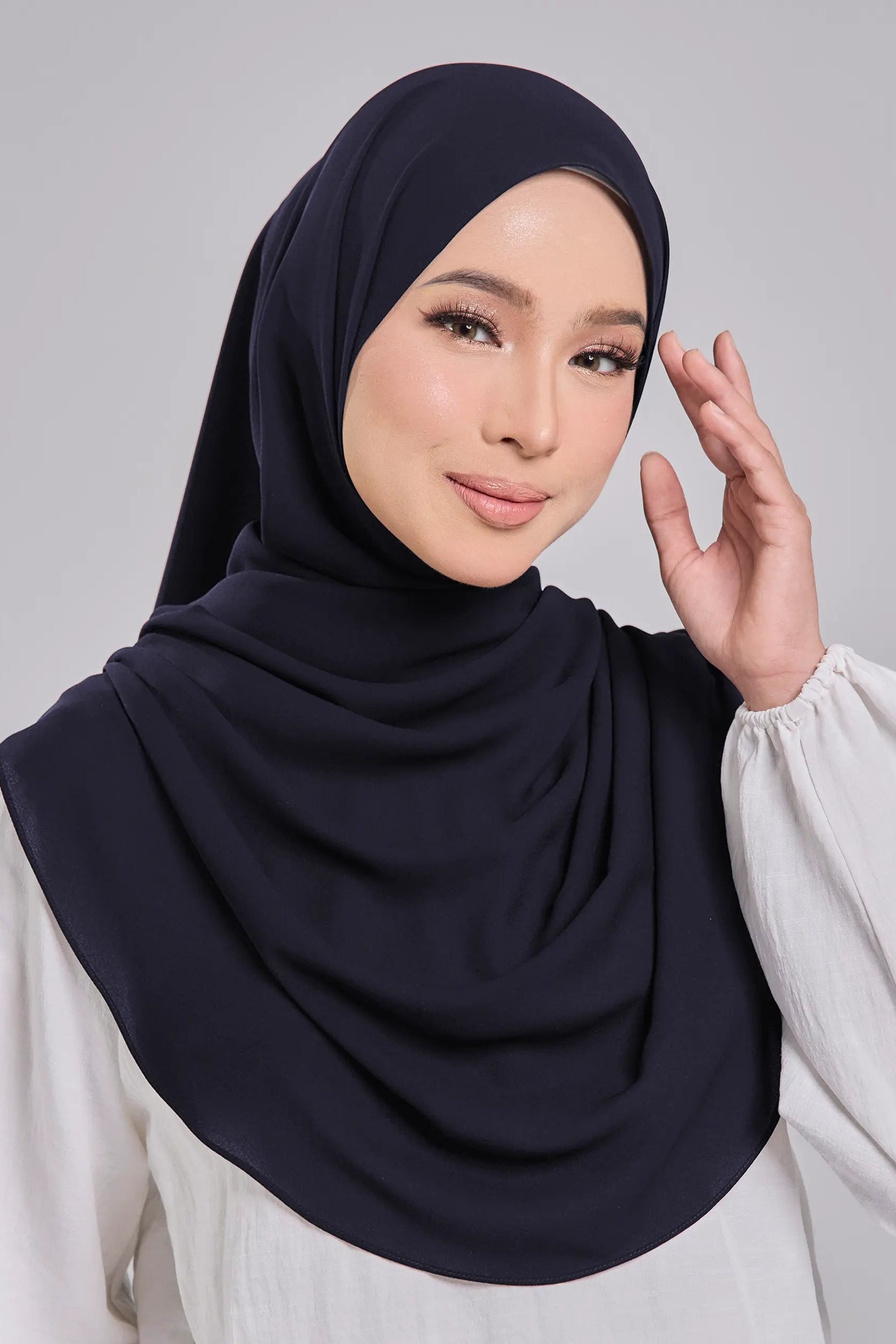 Woman wearing a navy hijab and white blouse against a gray background