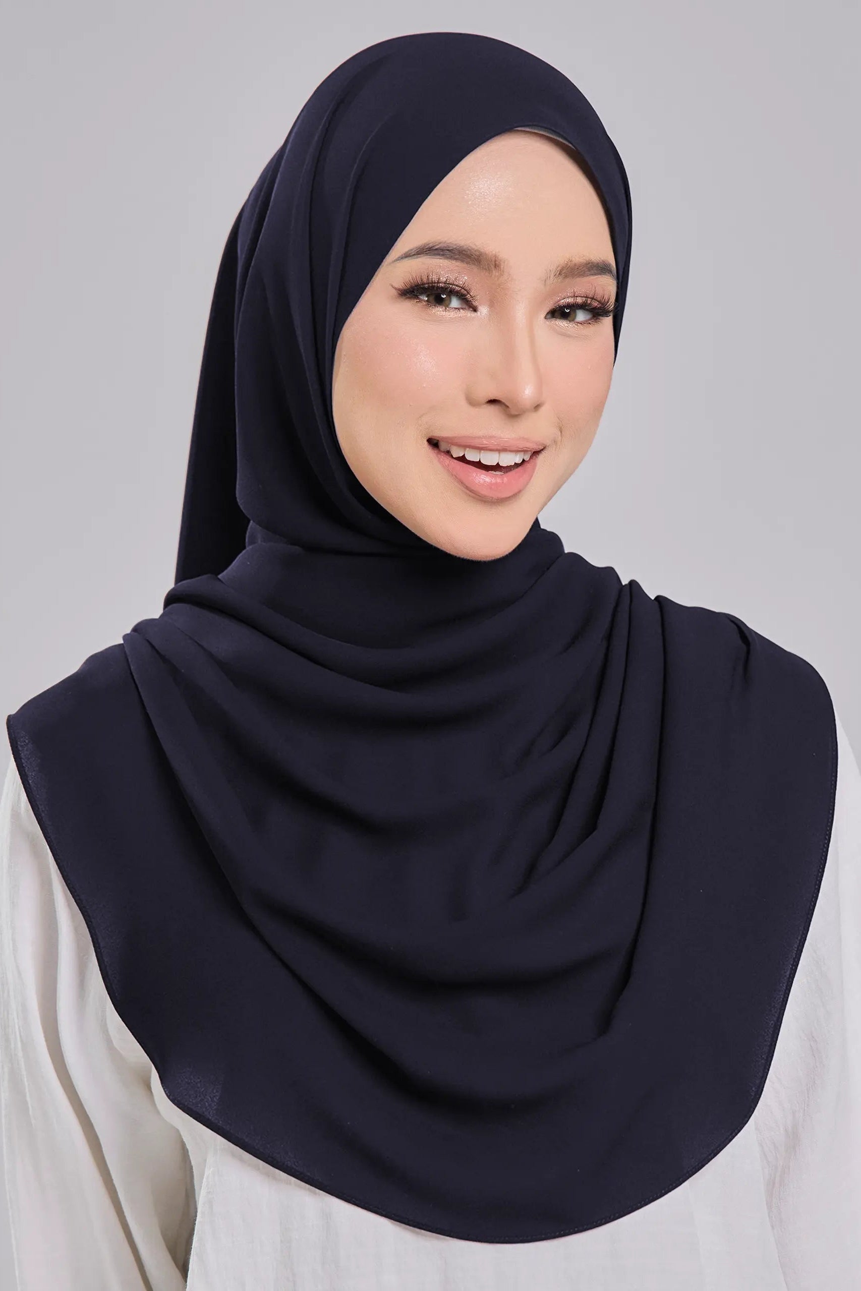 Woman wearing a navy hijab against a gray background