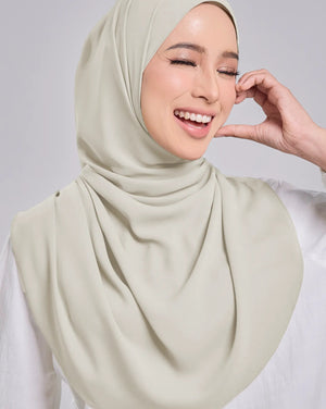 Woman wearing a light green hijab against a plain background