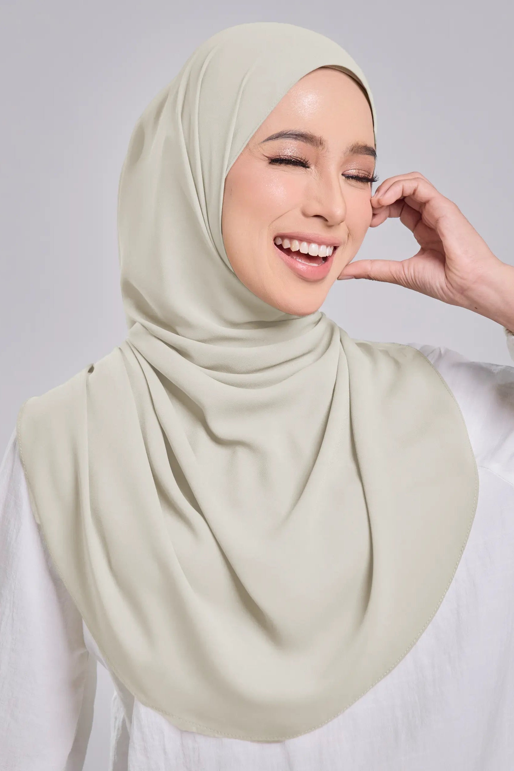 Woman wearing a light green hijab against a plain background