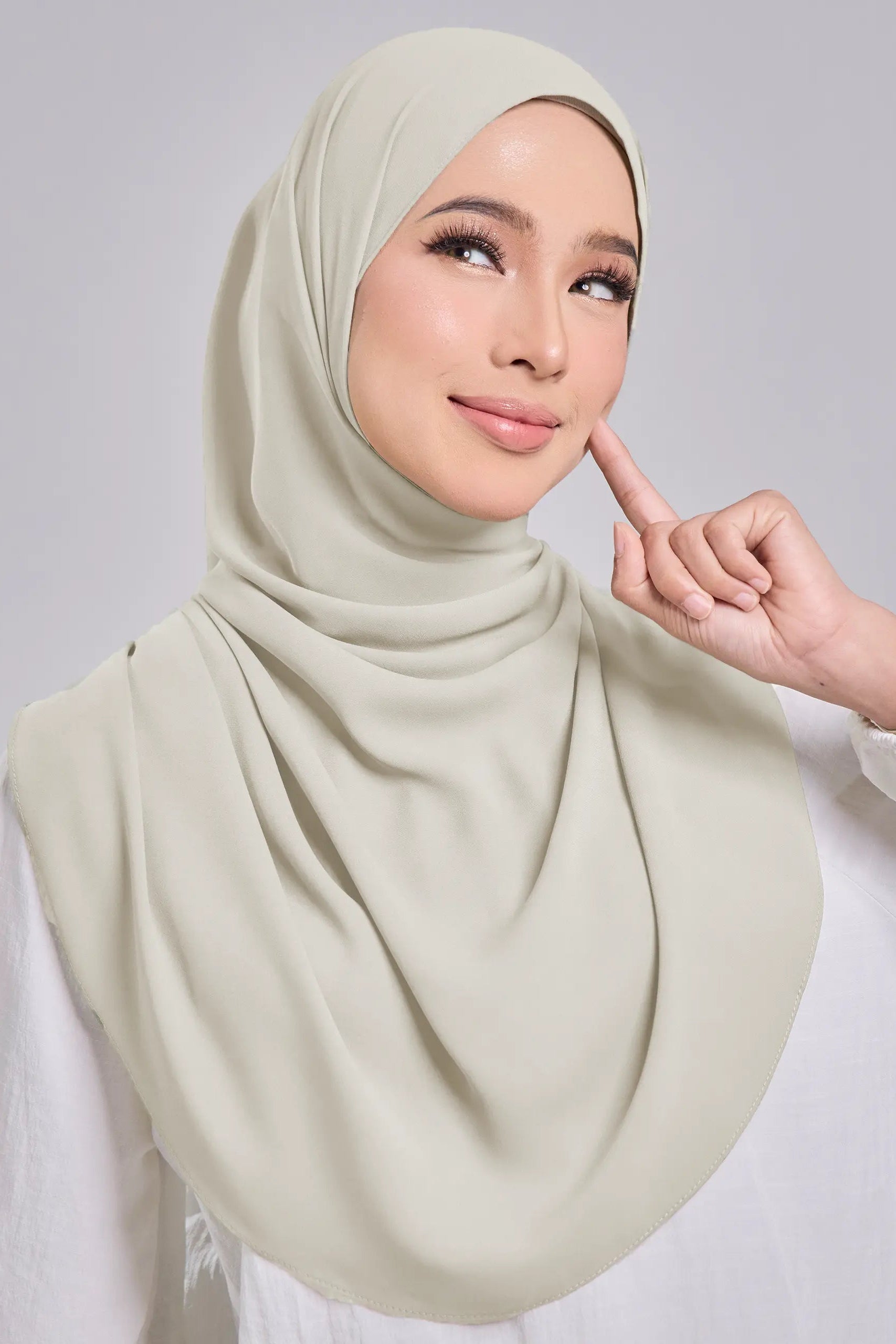 Woman wearing a light green hijab against a plain background