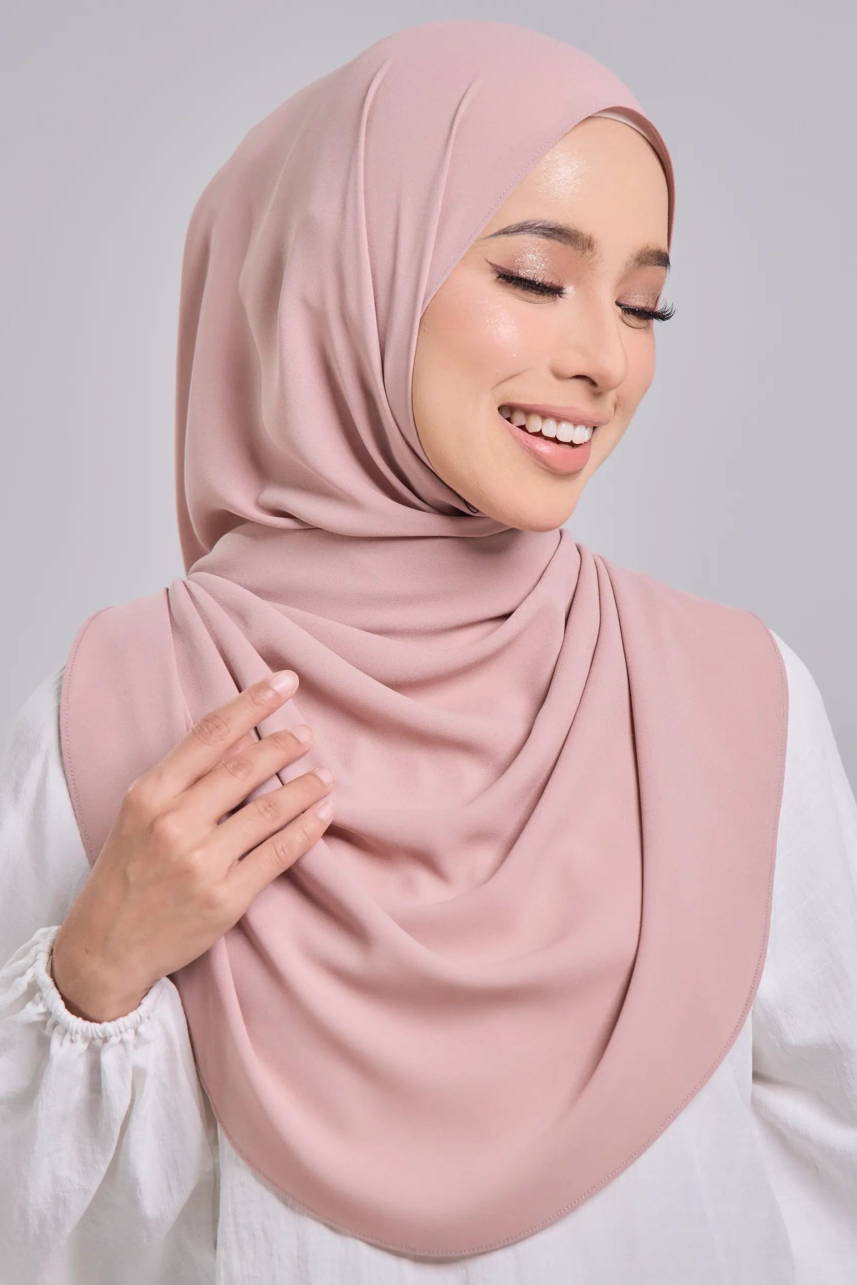 Woman wearing a pink hijab and white top on a gray background