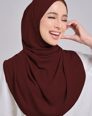 Woman wearing a maroon hijab and white shirt on a gray background