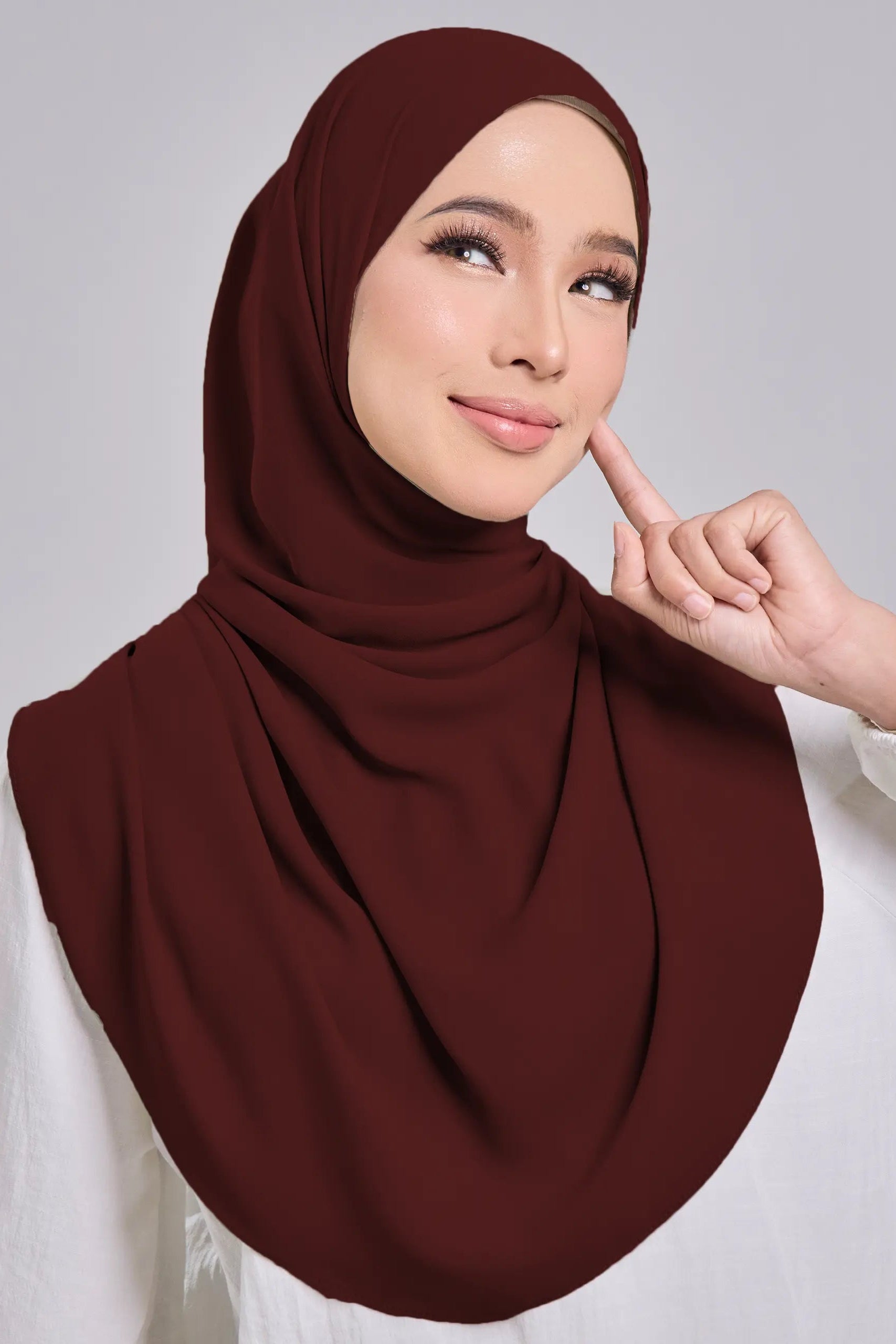 Woman wearing a brown hijab and white top on a gray background