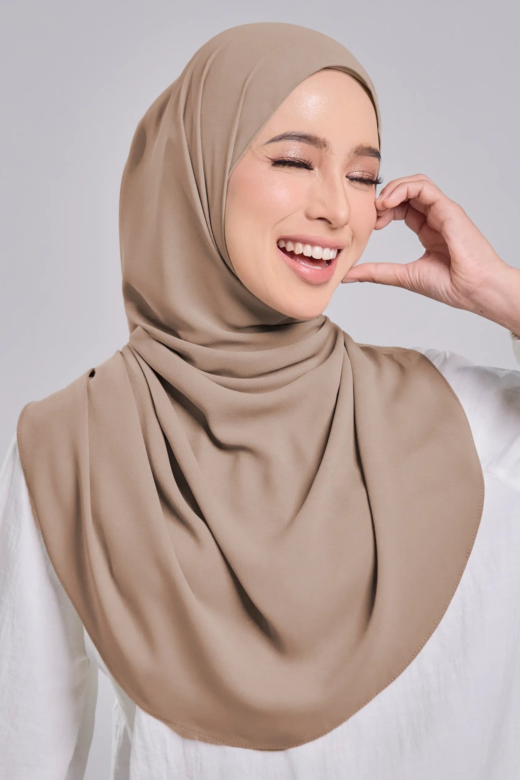 Woman wearing a beige hijab against a plain background