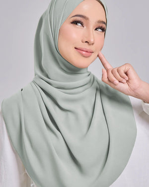Woman wearing a light green hijab against a plain background