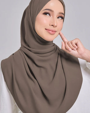Woman wearing a brown hijab and white top against a gray background