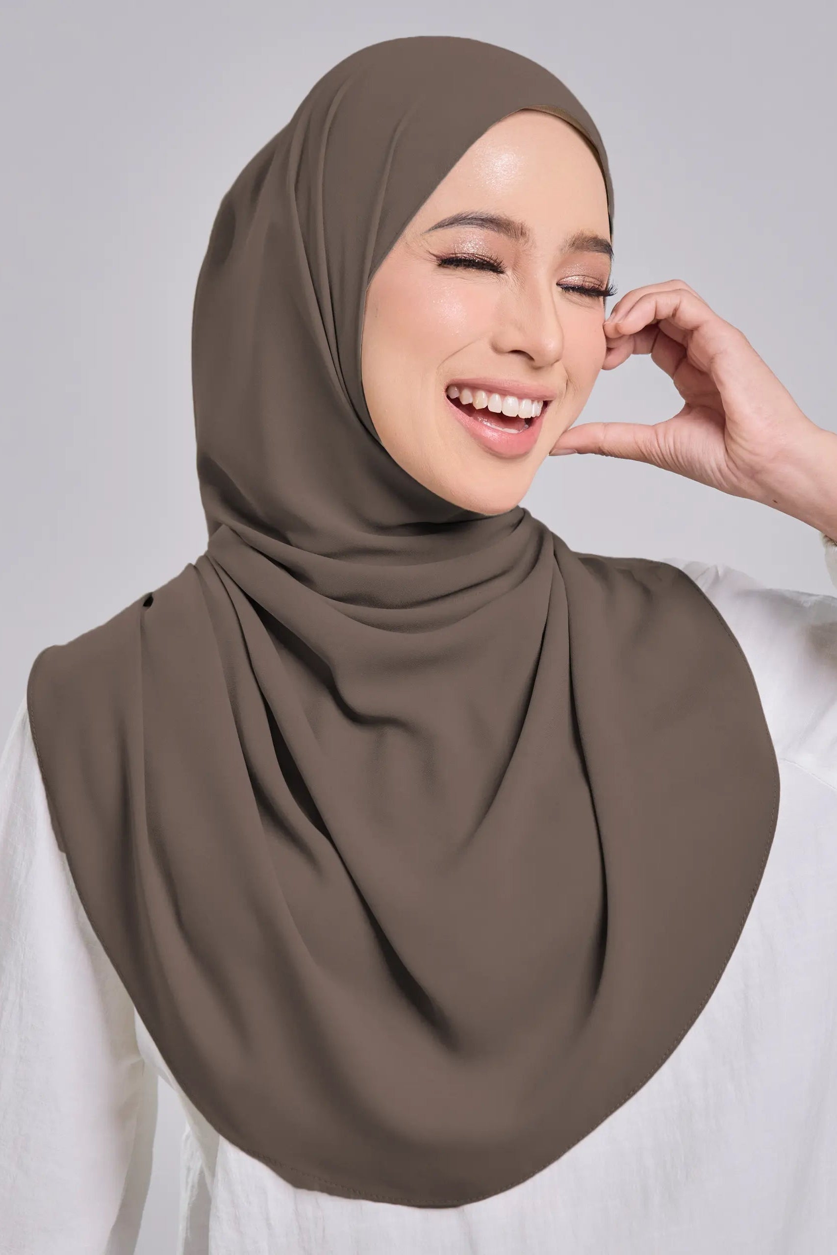 Woman wearing a brown hijab and white shirt against a gray background