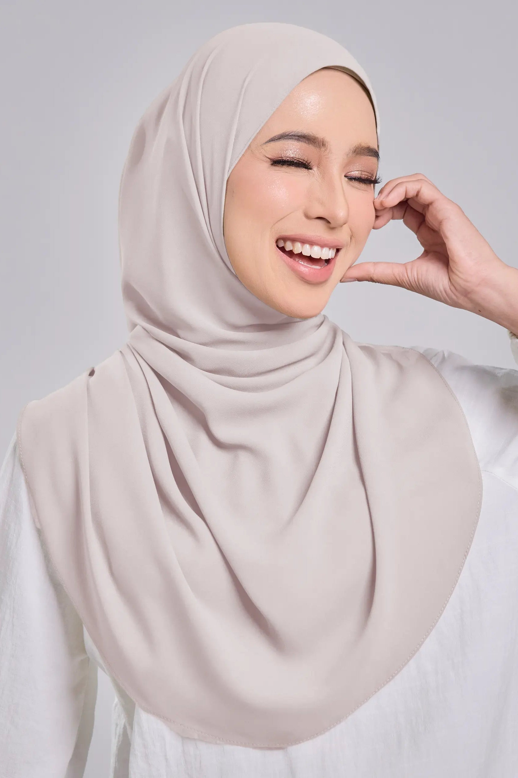 Woman wearing a beige hijab against a plain background