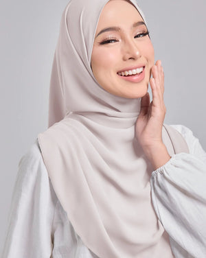 Woman wearing a beige hijab and white top against a light gray background