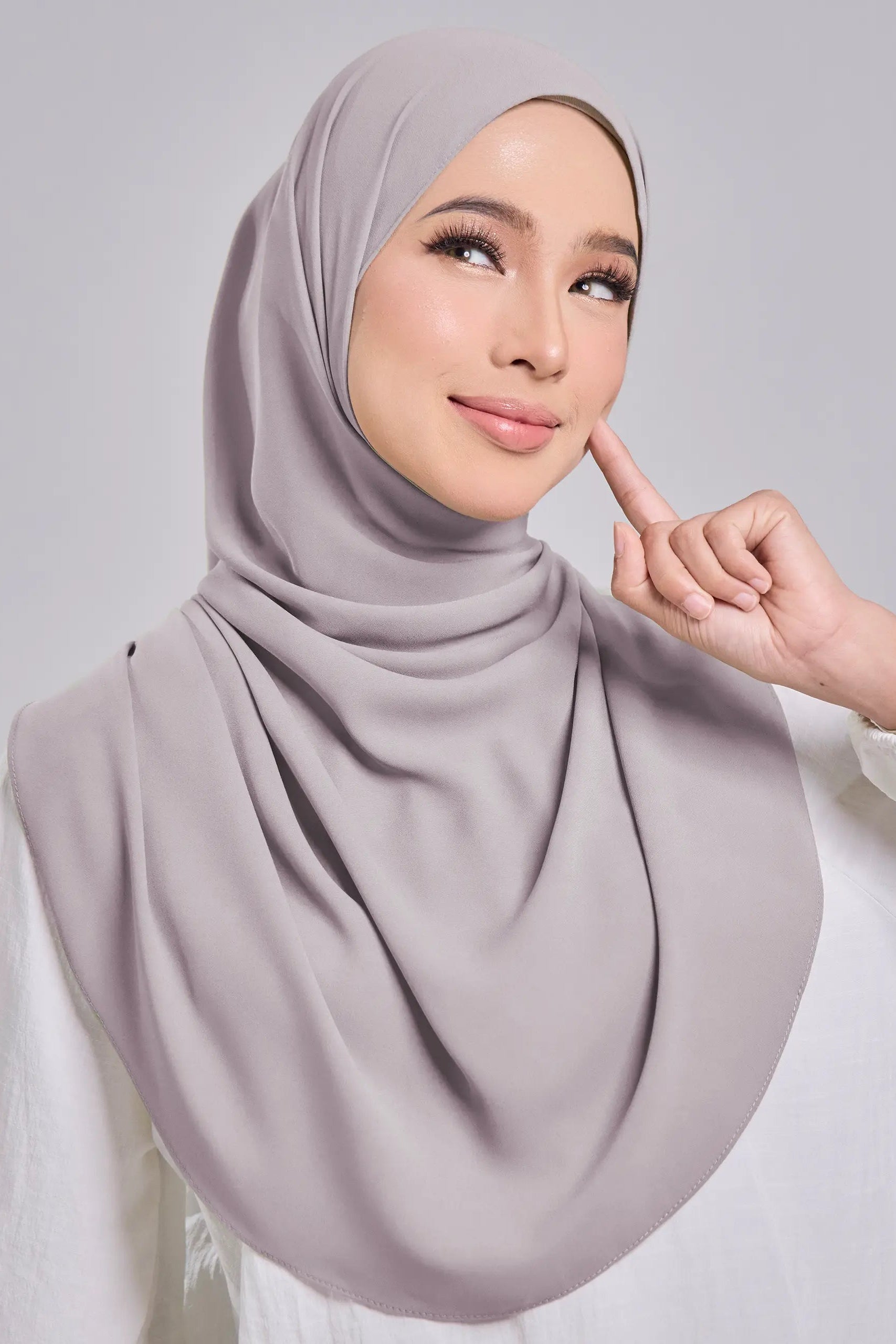 Woman wearing a light gray hijab against a plain background