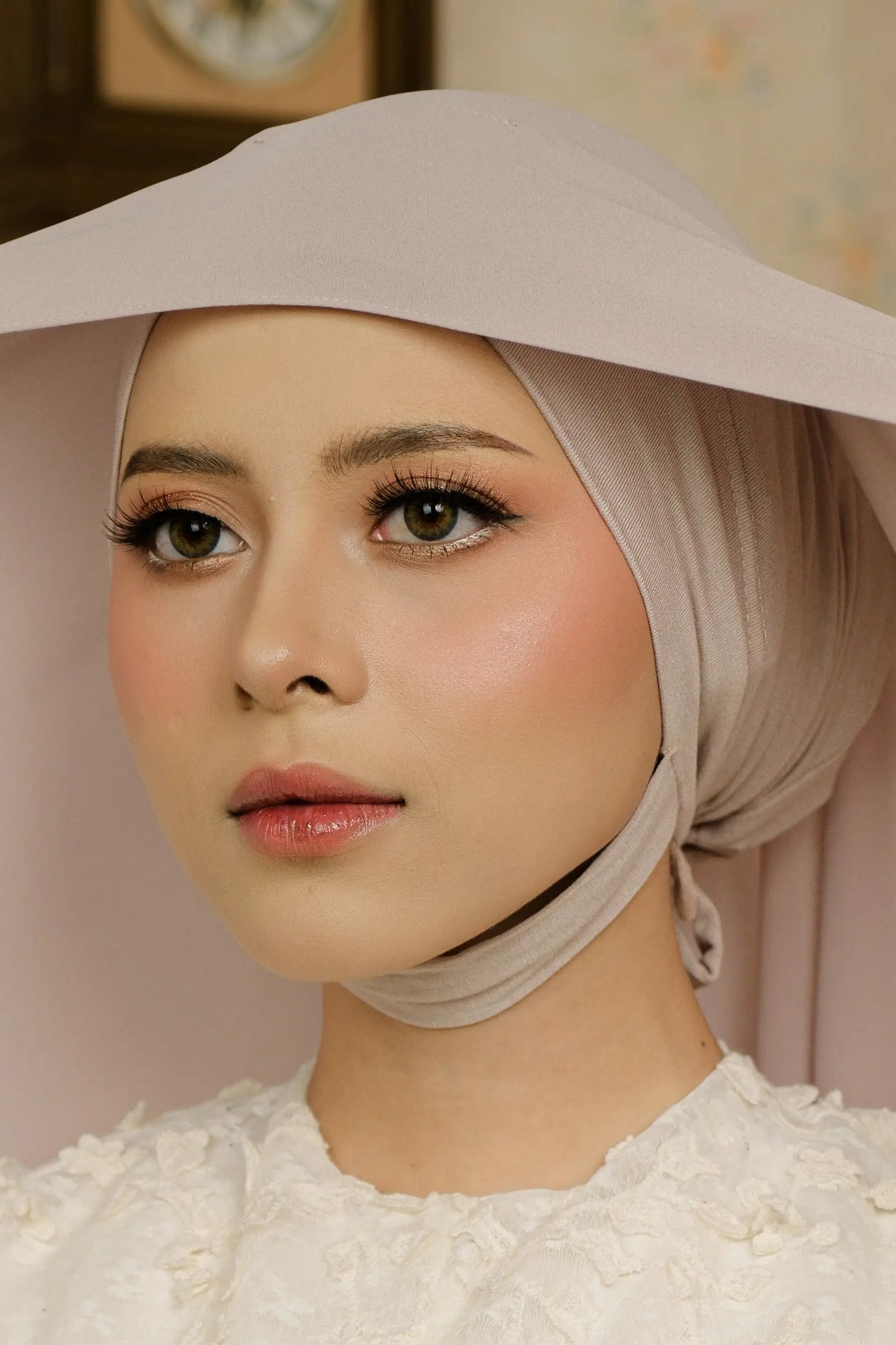 Woman wearing a beige hijab and white top with a decorative pattern.