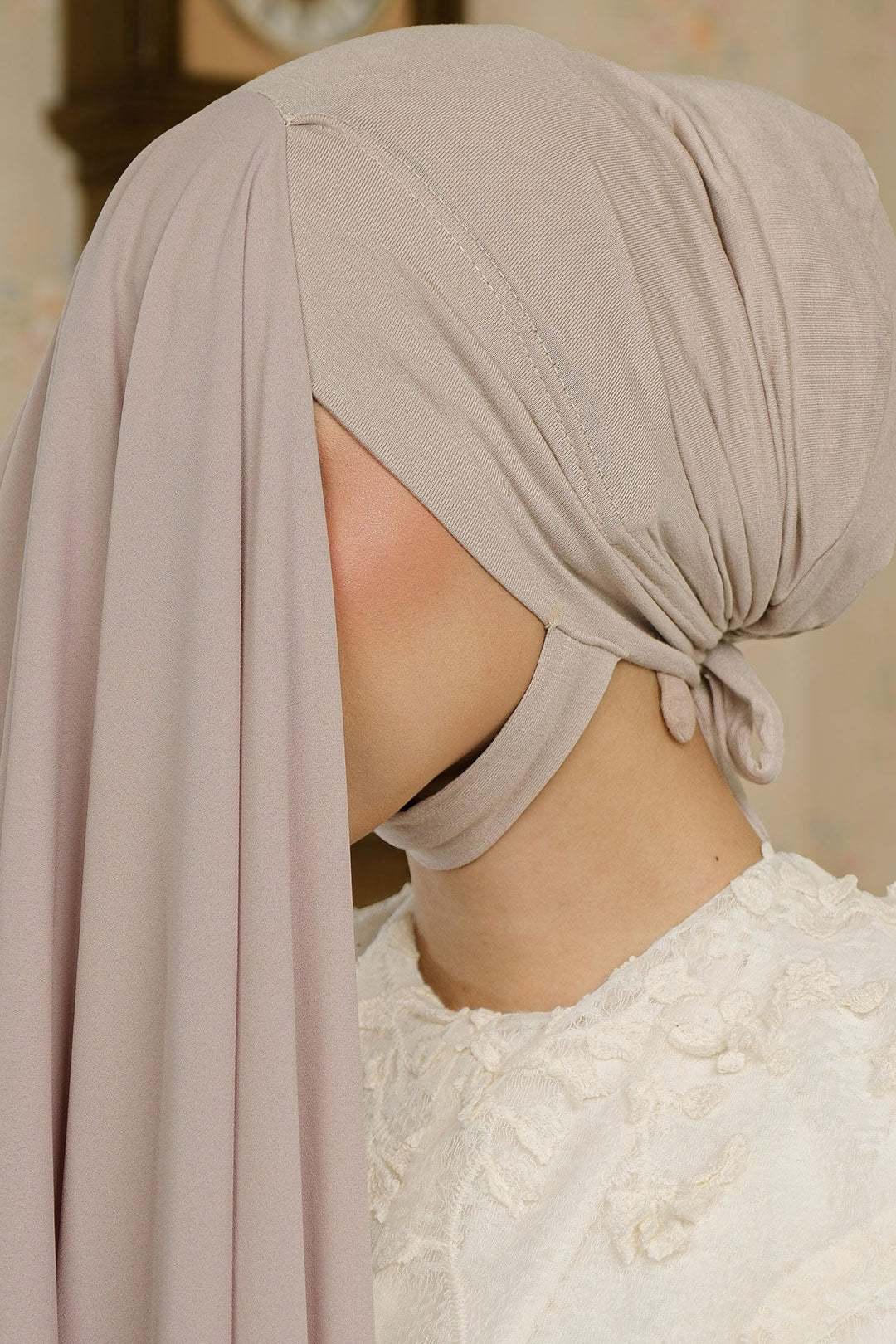 Person wearing a beige headscarf with a decorative clock in the background