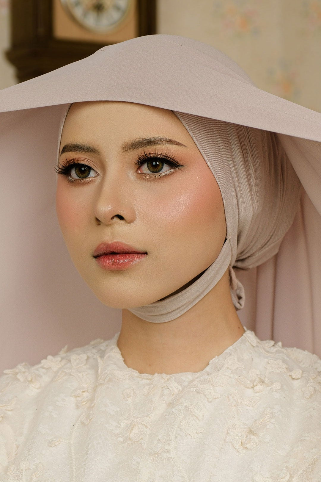 Woman wearing a light-colored headscarf and white garment indoors.