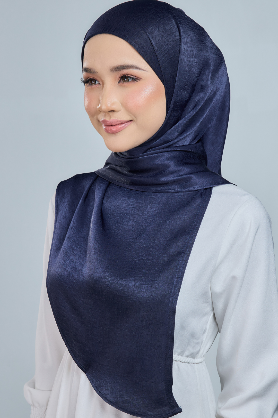 Woman wearing a navy hijab against a light gray background