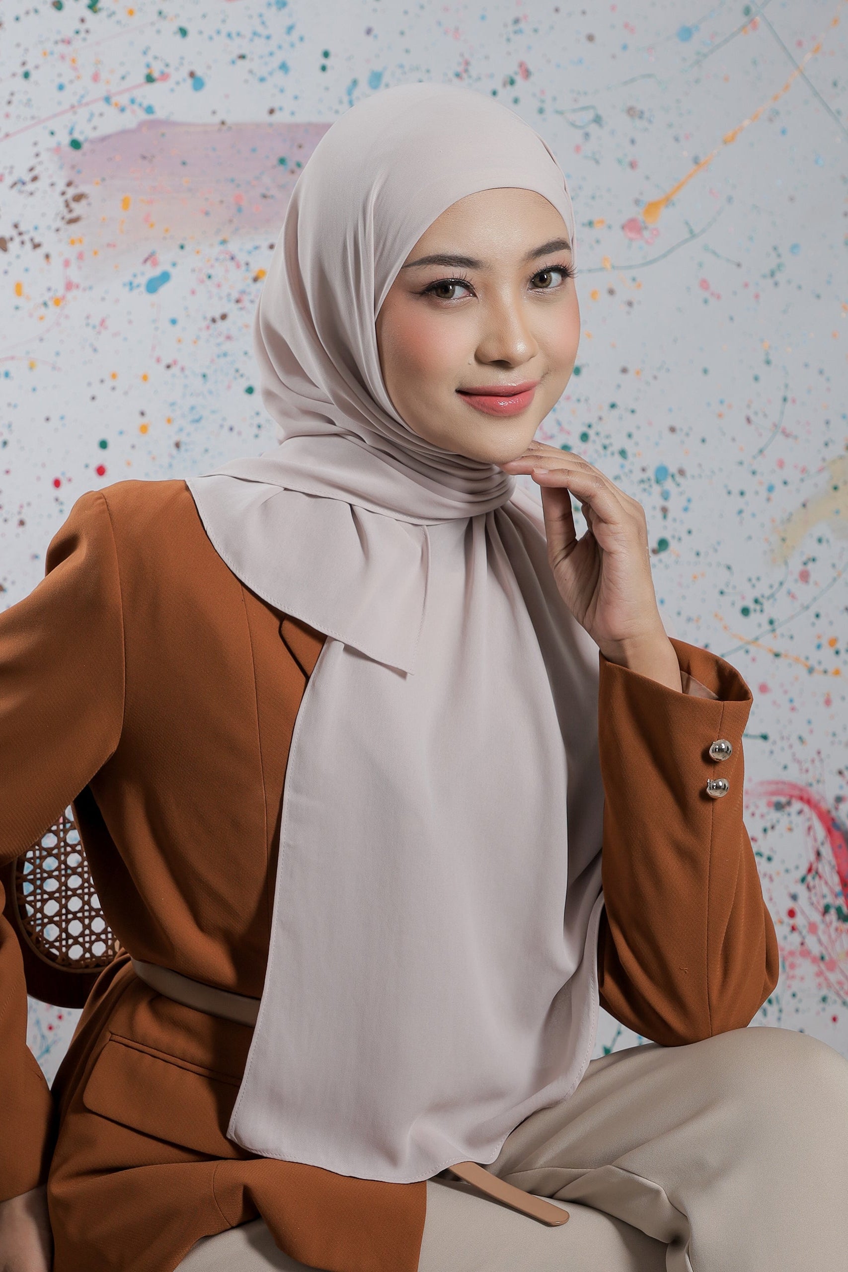 Woman wearing a brown outfit with a beige hijab against a colorful abstract background