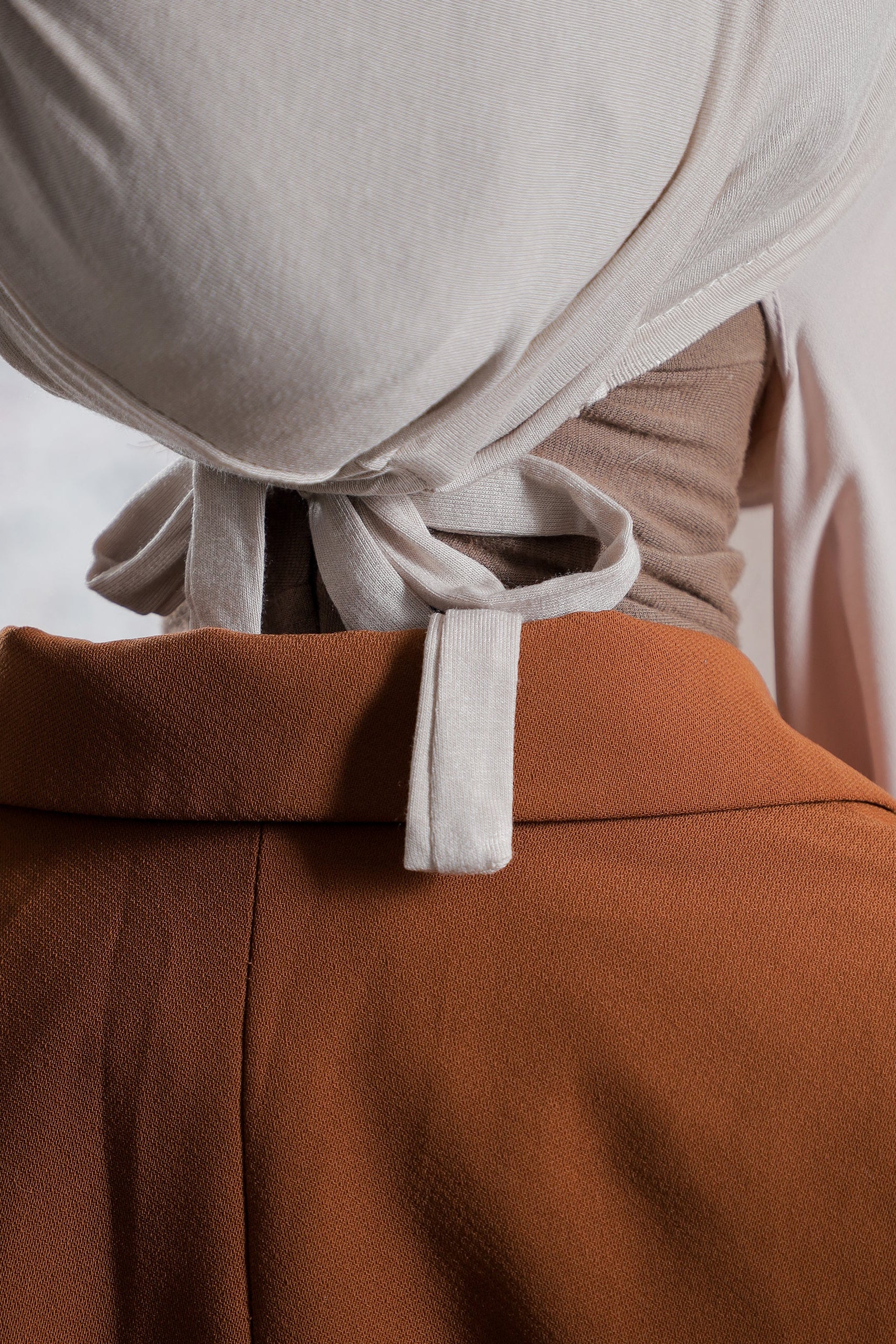 Close-up of a person wearing a beige top and brown pants with a white belt.