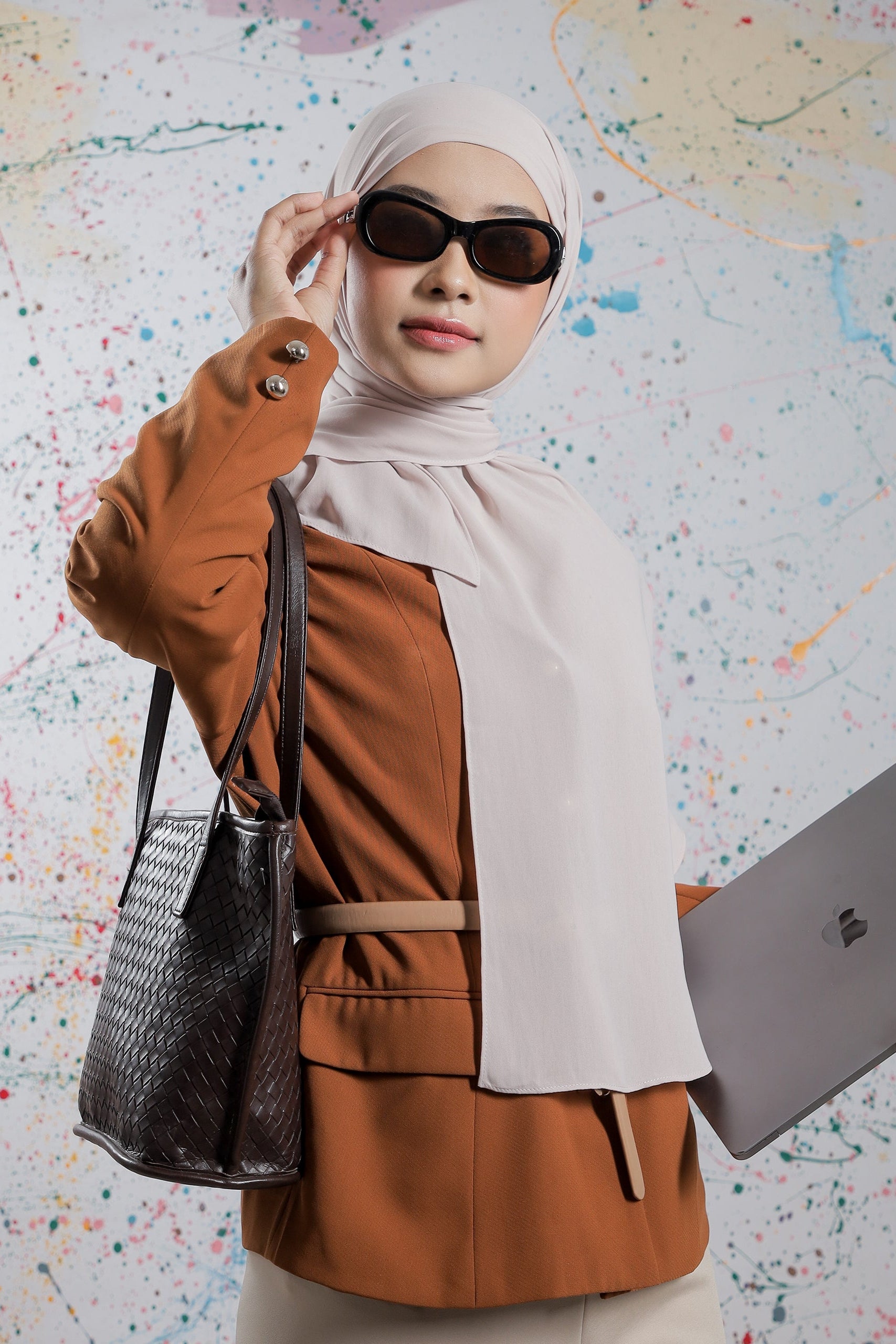 Woman holding a laptop and a handbag against a colorful abstract background