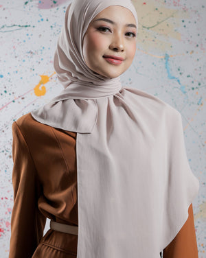 Woman wearing a beige hijab and brown outfit against a colorful abstract background