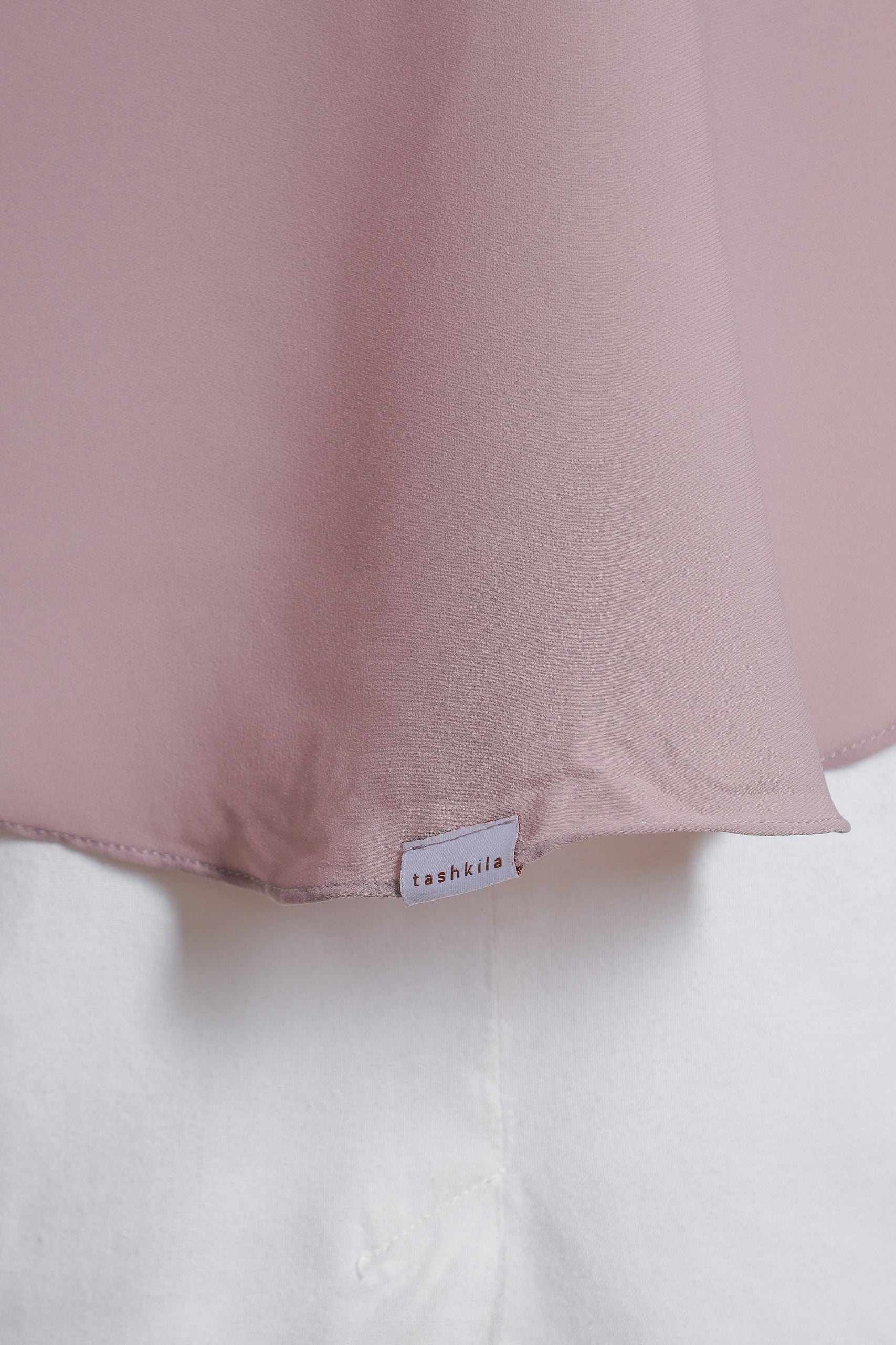 Close-up of a pink fabric with a visible brand label on a white background