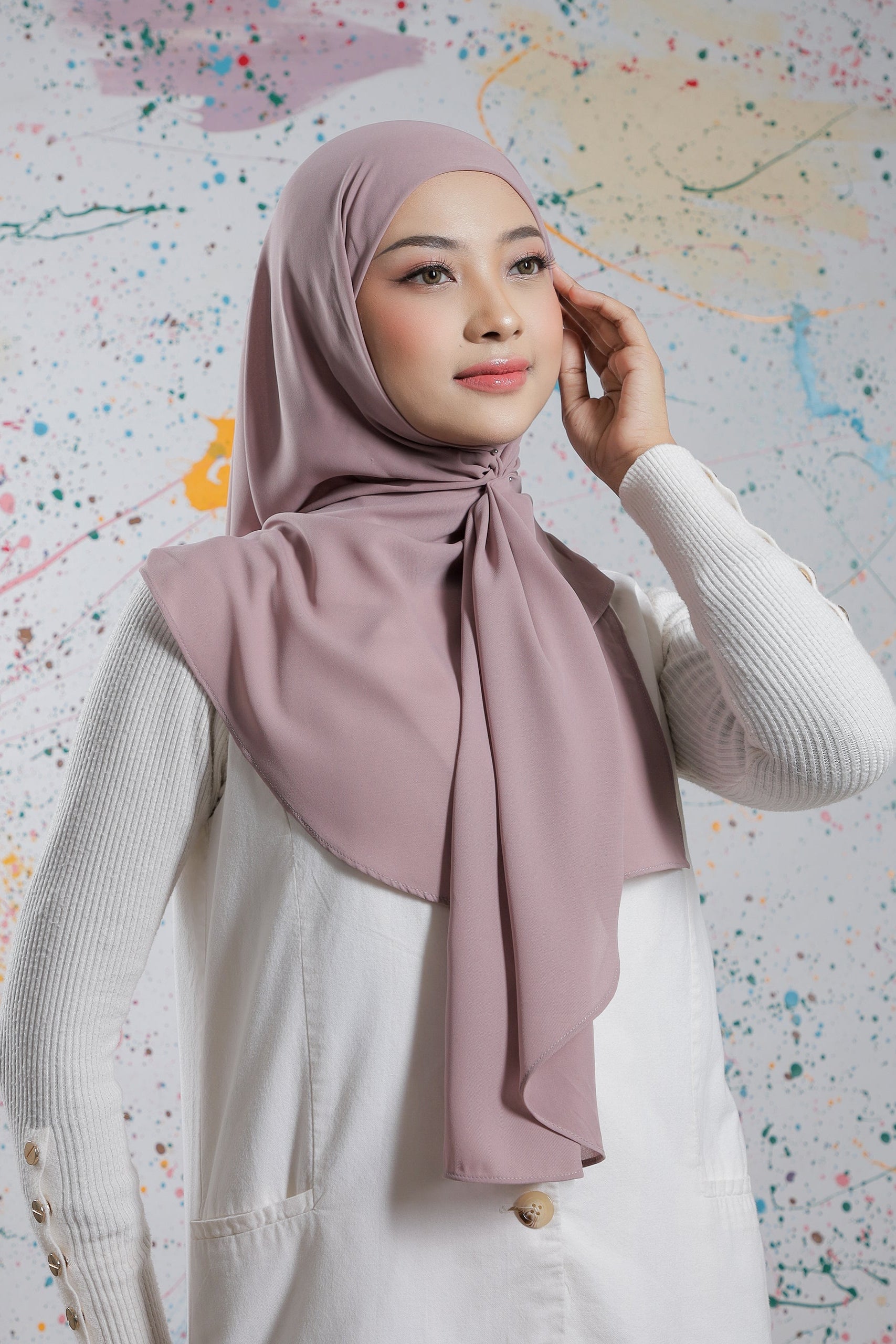 Woman wearing a light pink hijab against a colorful abstract background