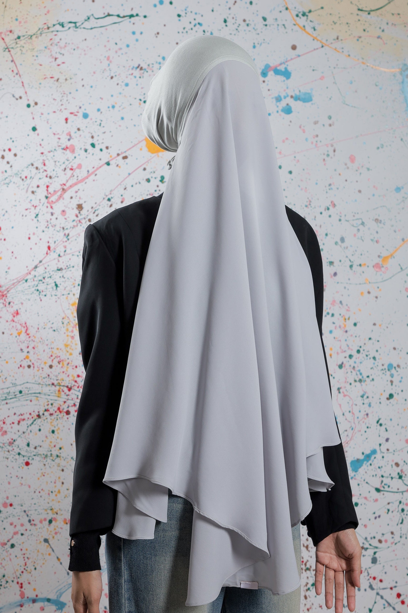 Person wearing a white hijab and black top against a colorful abstract wall.