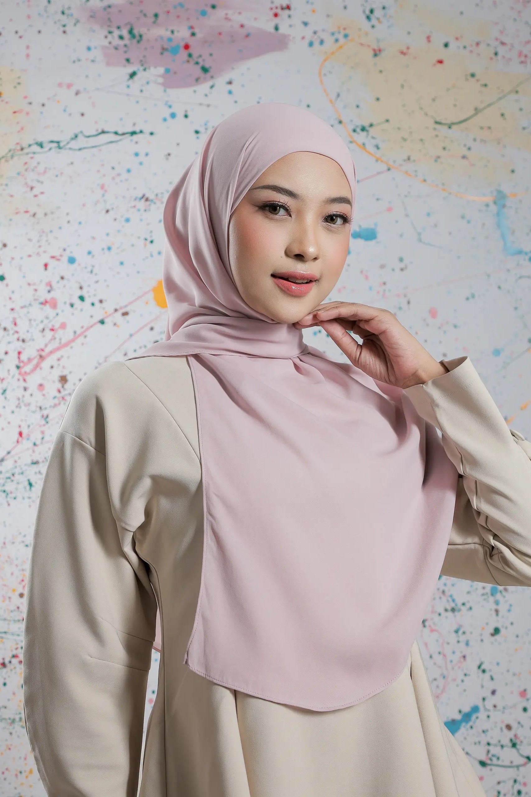 Woman wearing a light pink hijab and beige outfit against a colorful abstract background