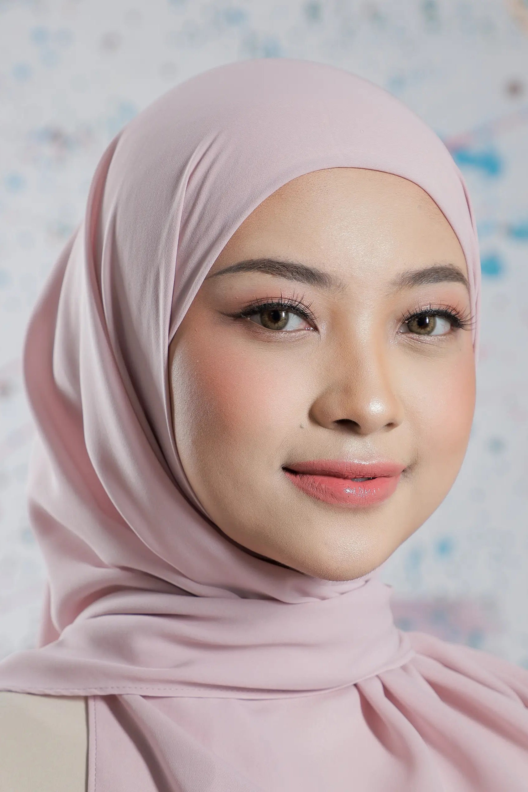 Woman wearing a light pink hijab against a patterned background