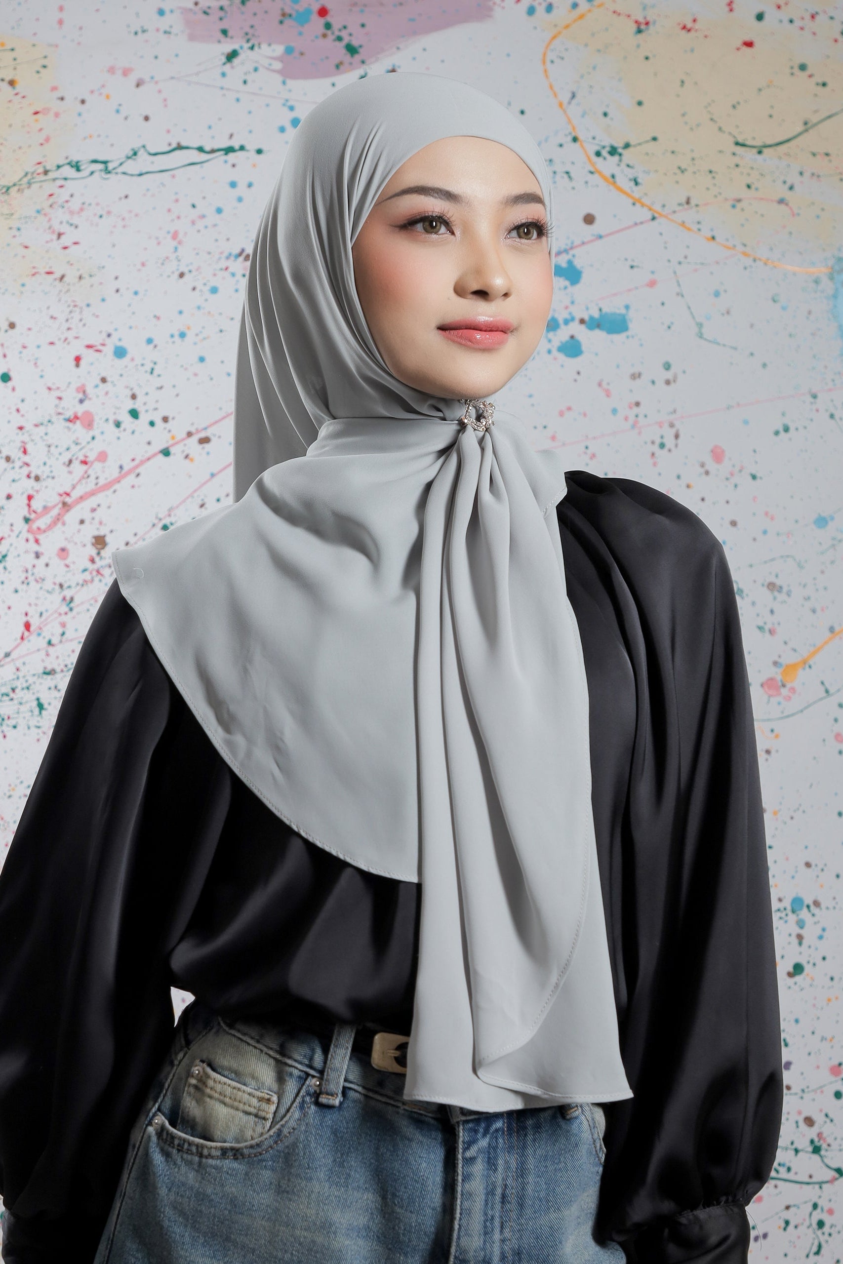 Woman wearing a gray hijab and black top against a colorful abstract background